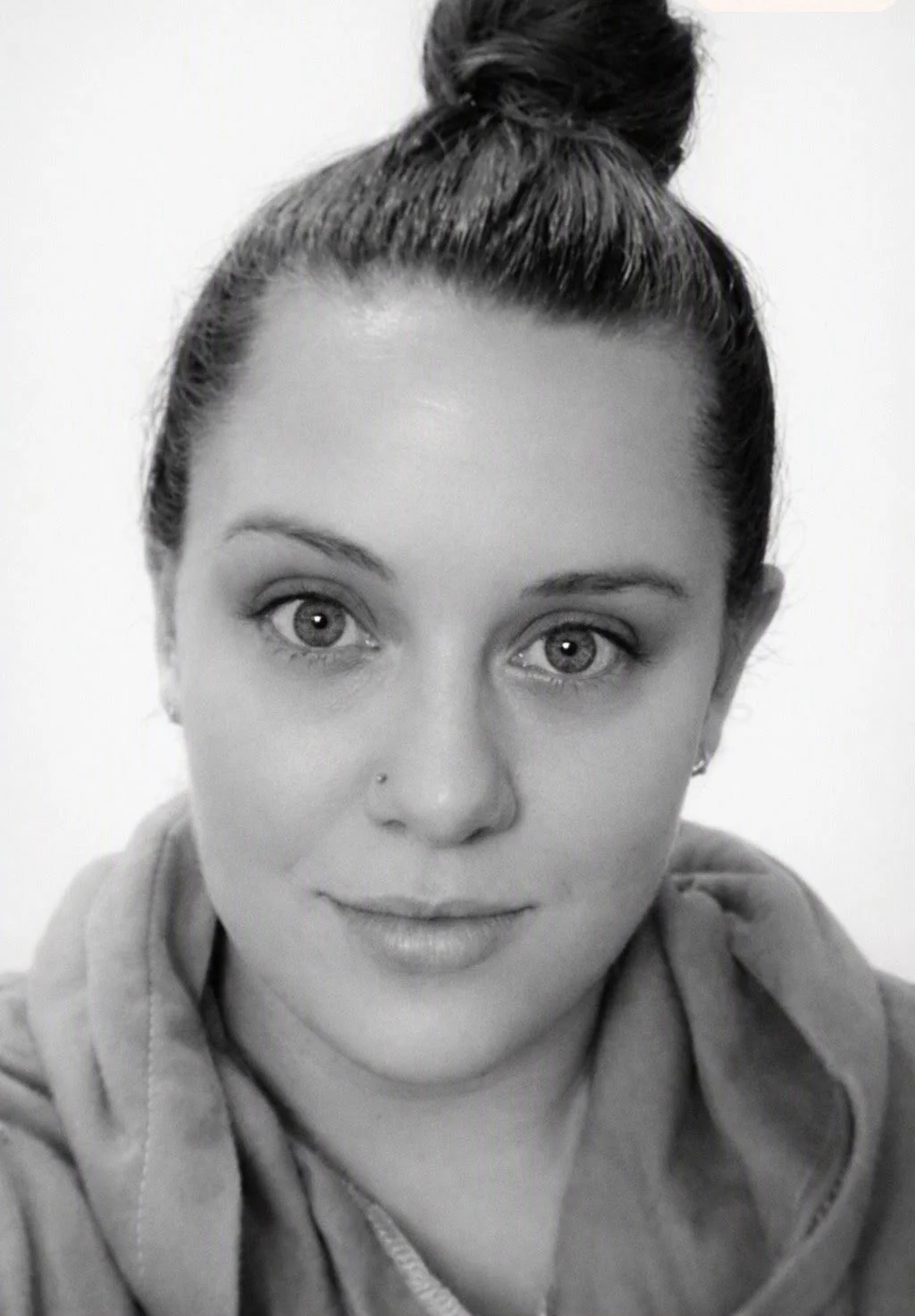 Black and white close-up portrait of a woman with her hair in a bun, wearing a hoodie, looking directly at the camera.