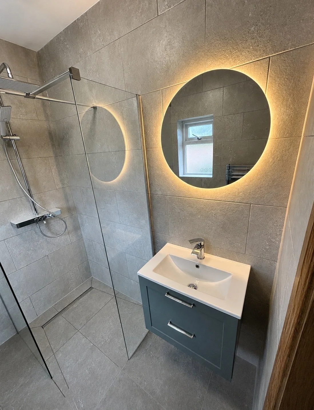Modern grey bathroom with a walk-in shower, floating vanity and illuminated mirror.