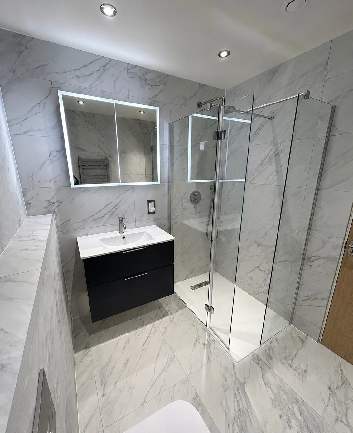 Elegant marble-effect bathroom with a walk-in shower, dark vanity and illuminated mirror.