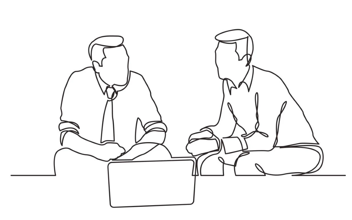 Two men sitting at a table, looking at a laptop, engaging in a discussion or meeting.