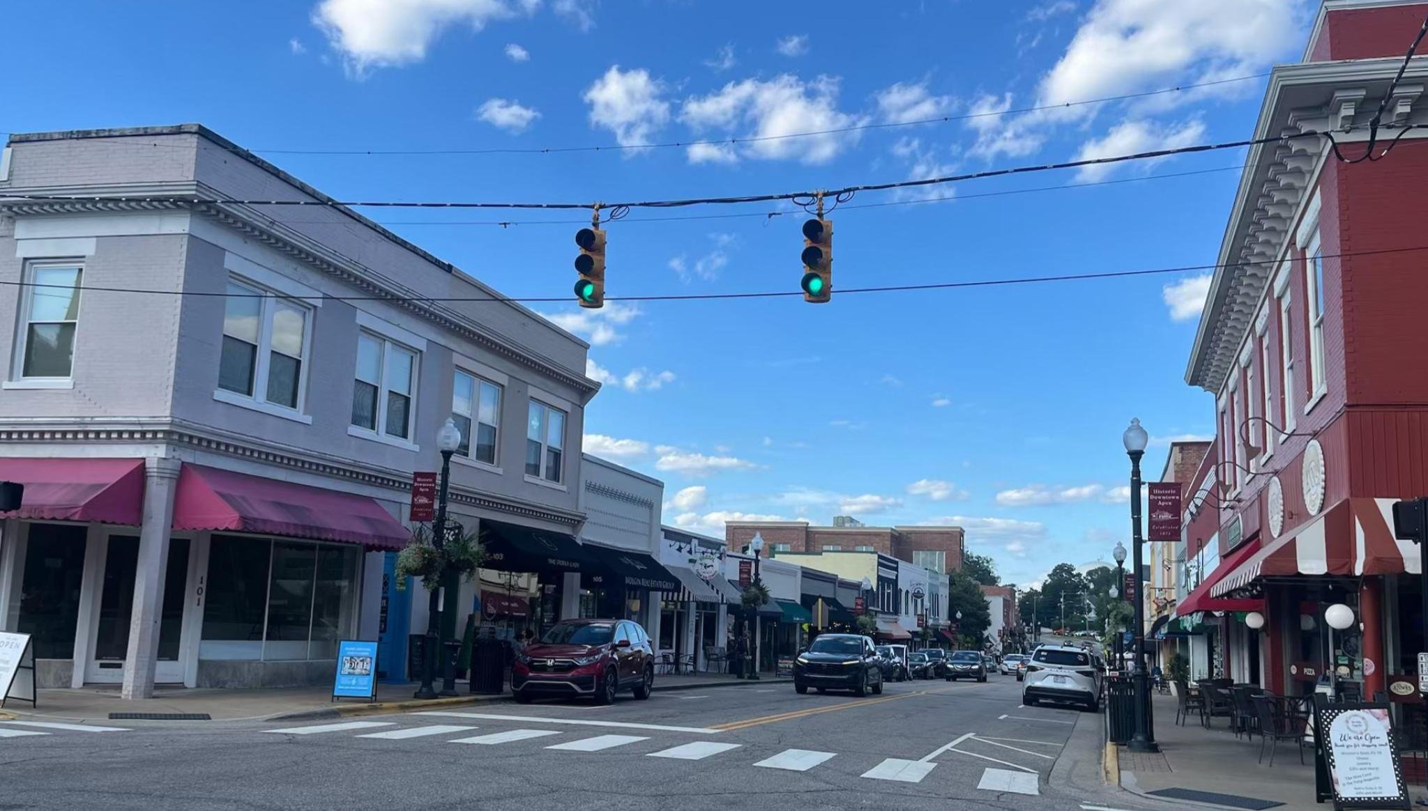 Downtown street scene with buildings, parked cars, and green traffic lights in clear weather.
