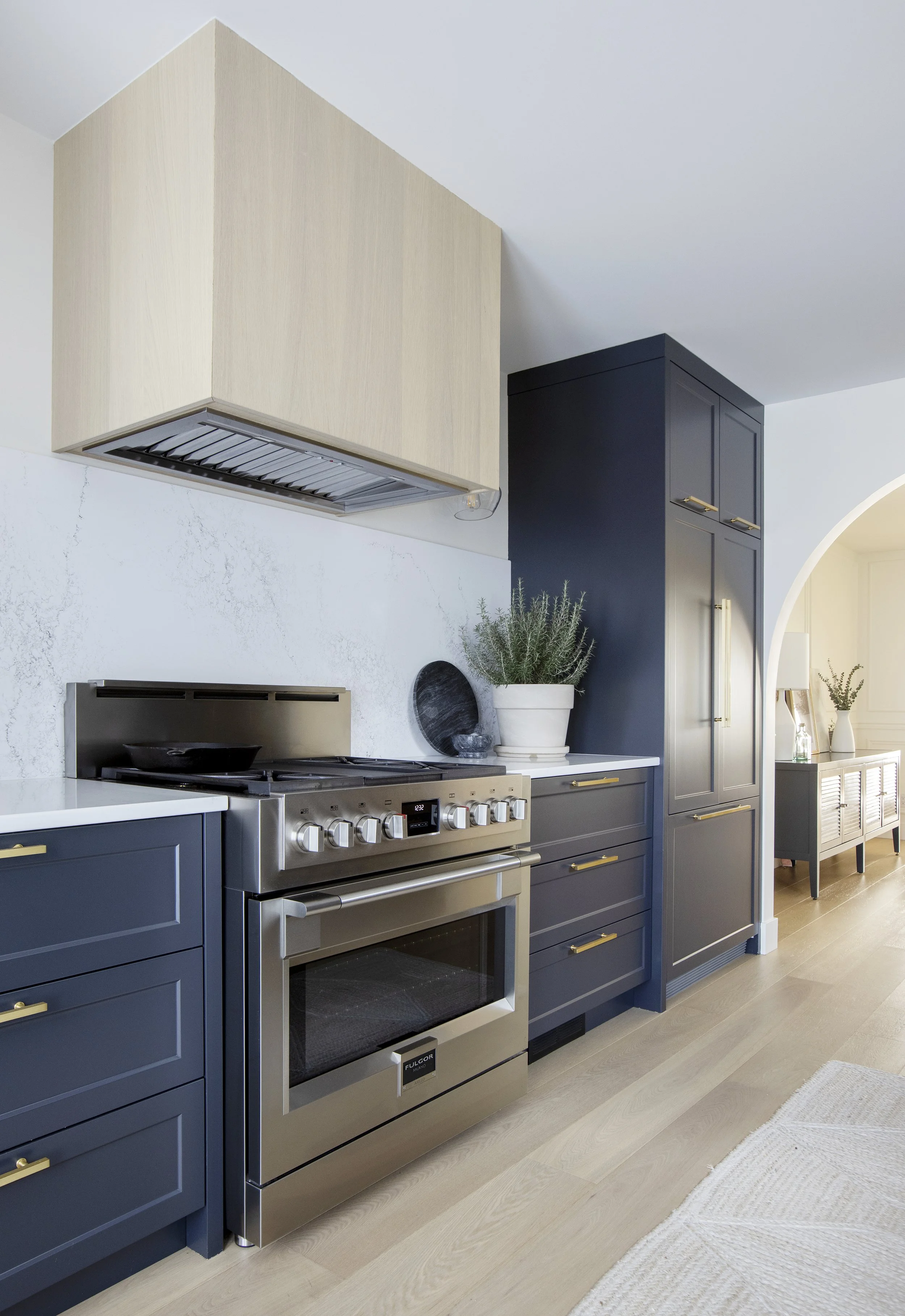 Modern kitchen with navy blue cabinets, stainless steel oven, blue cabinetry, and white countertops, with a potted plant on the counter.