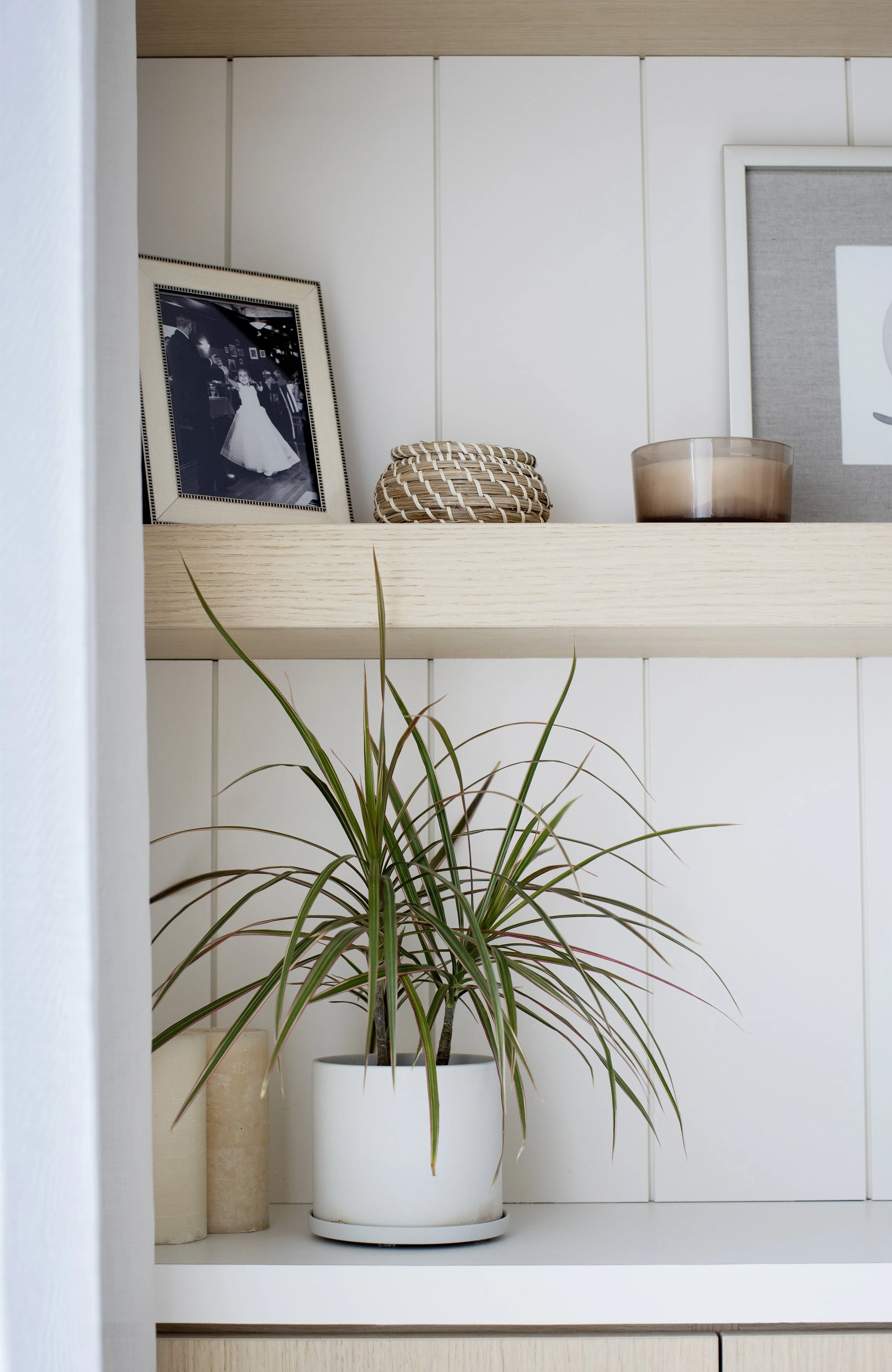 Indoor white shelf with green houseplant in a white pot, framed black-and-white photograph of a dancing couple, two pottery vases, and a brown glass container.