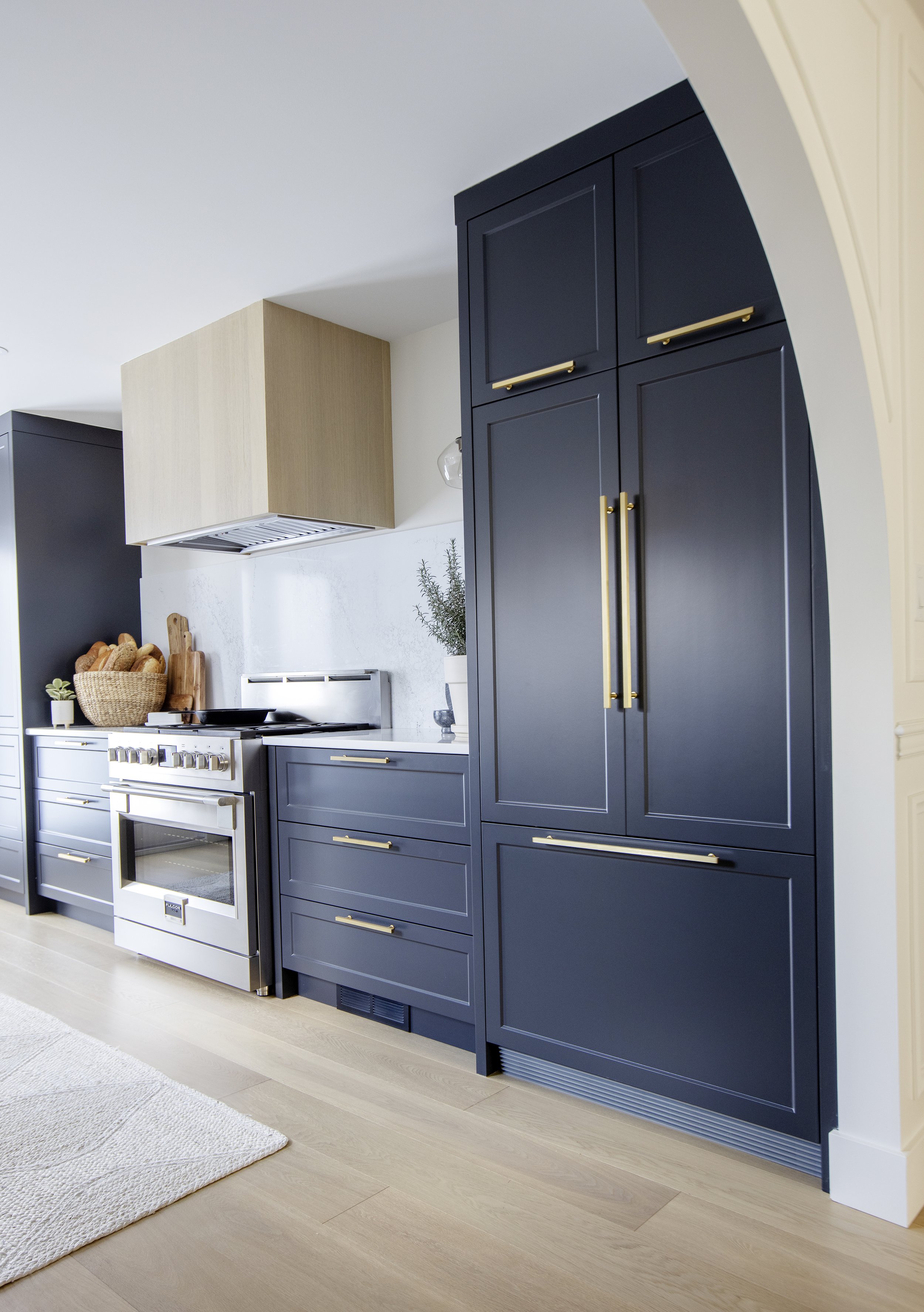Kitchen with dark blue cabinets, gold handles, stainless steel stove, and light wood flooring.