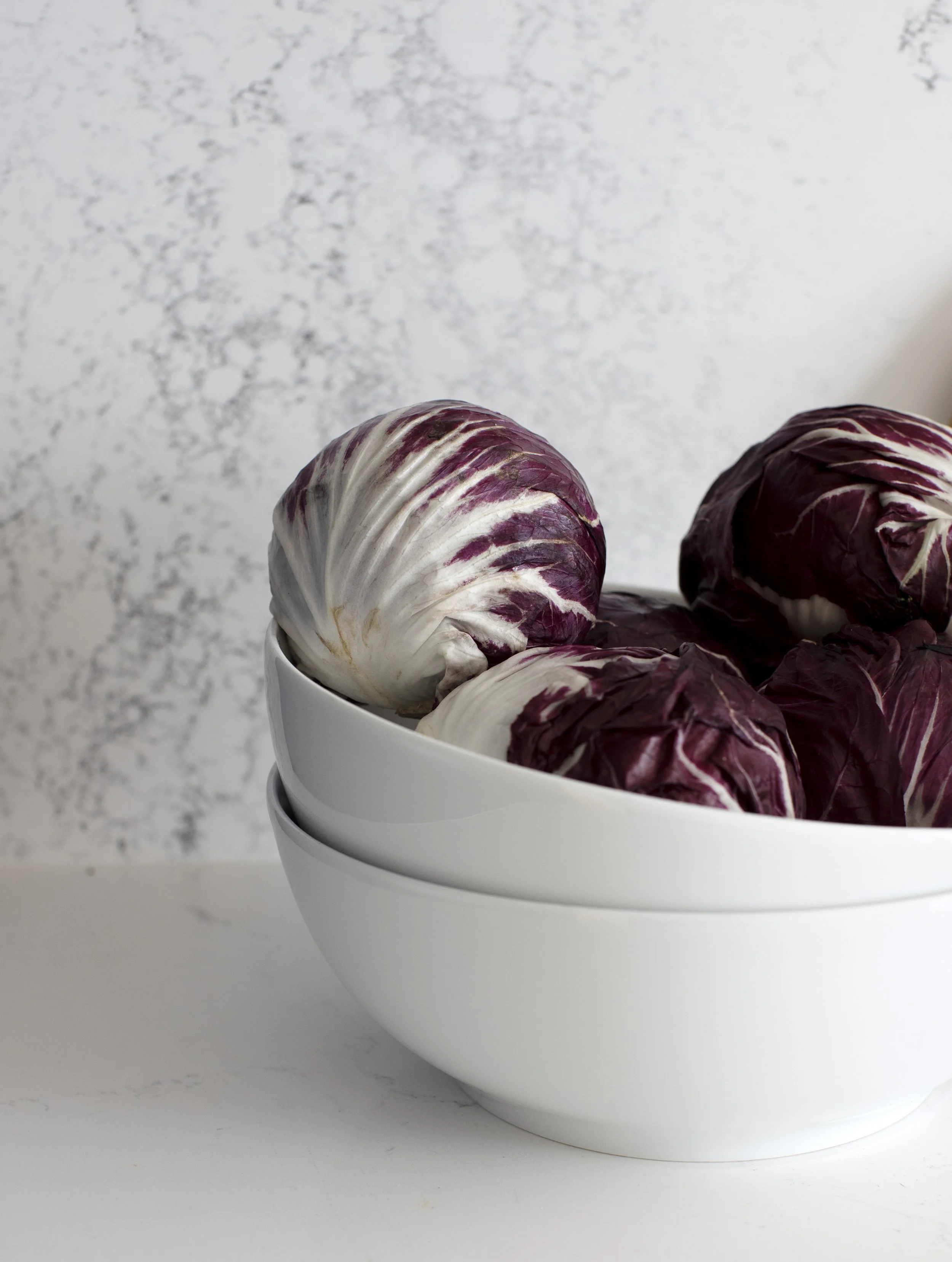 Close-up of a white bowl filled with red and white radicchio at a marbled surface.