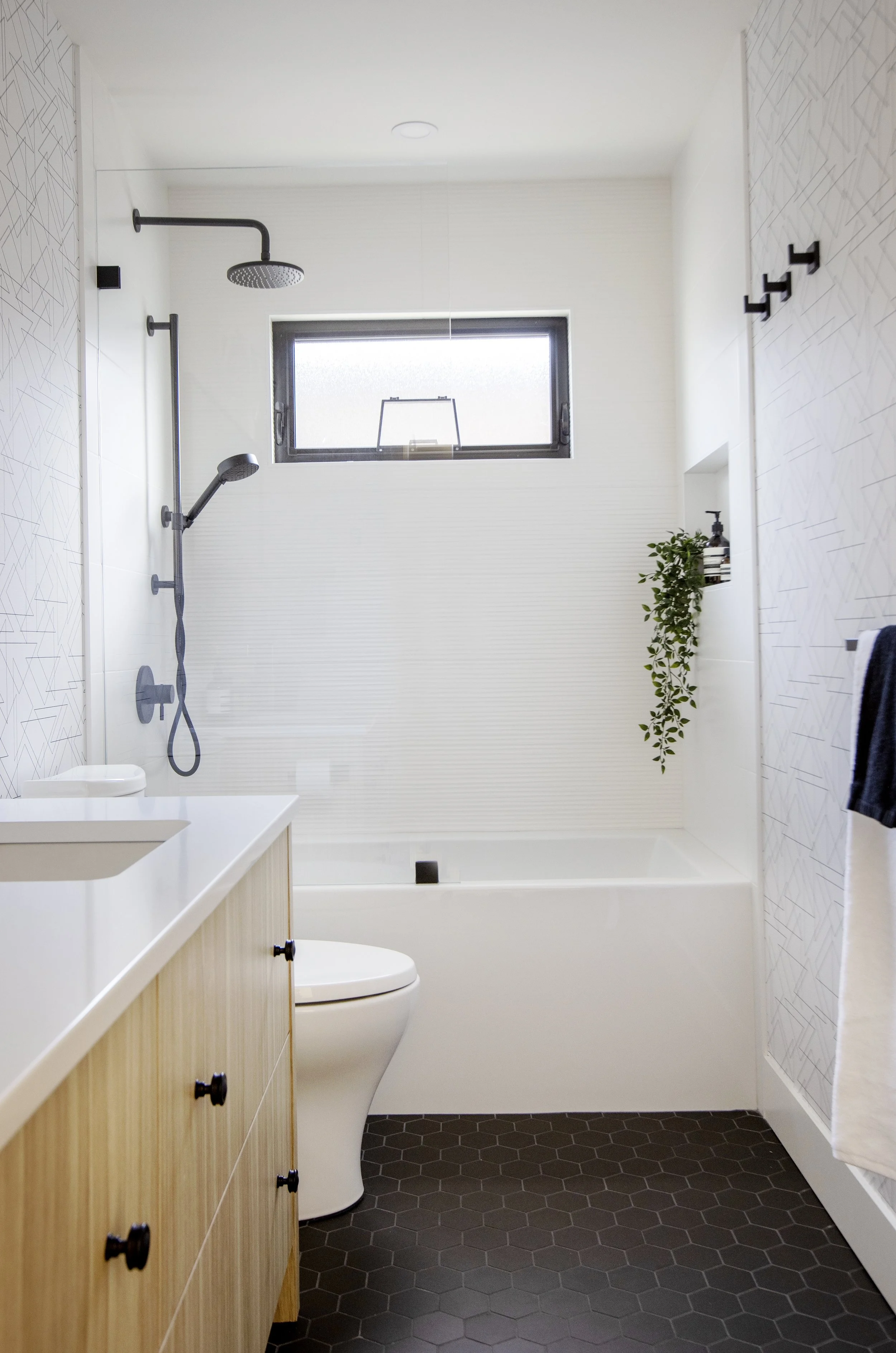 Modern bathroom with white walls, black fixtures, a window, a plant shelf, and a toilet