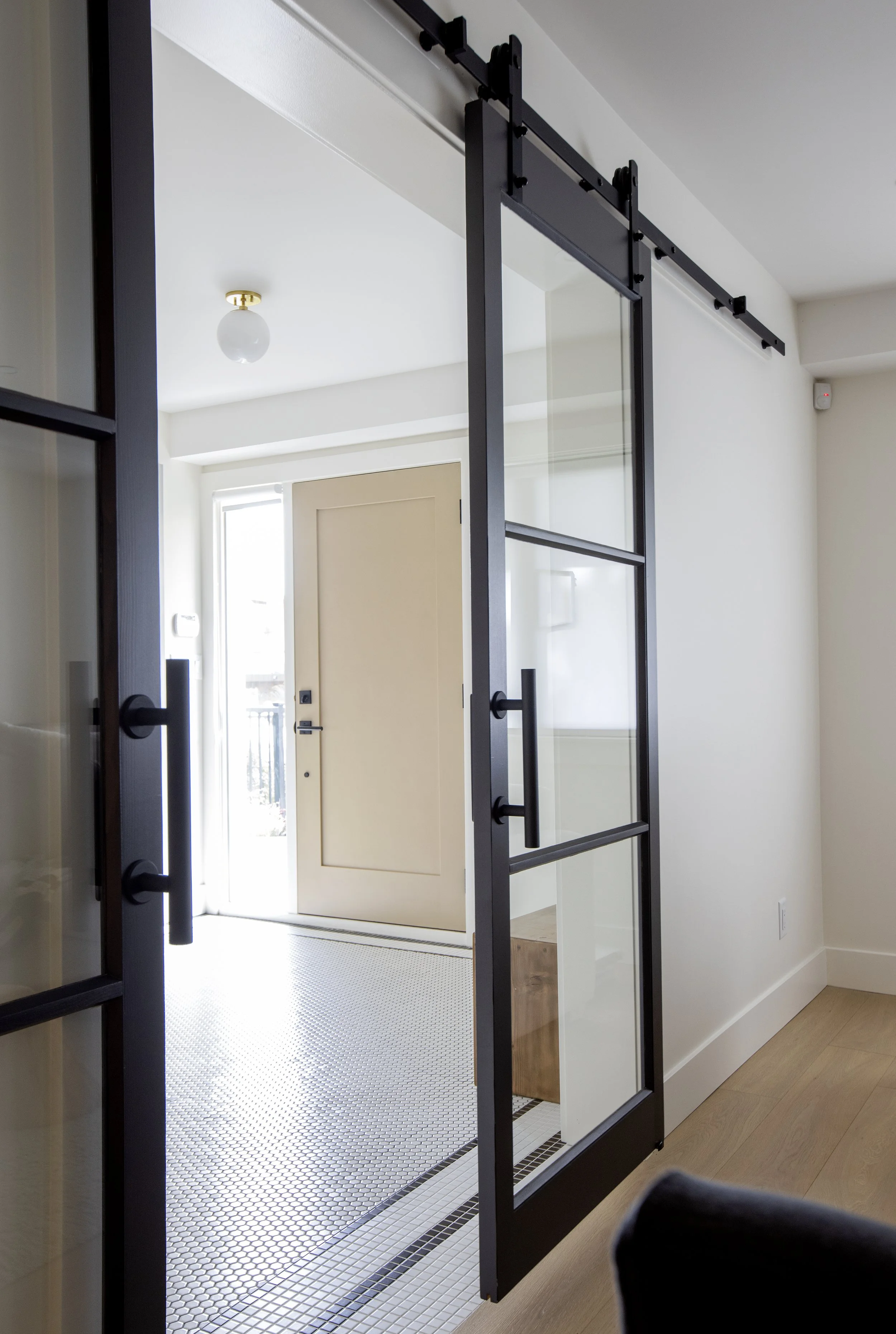 View of a modern home interior with a glass sliding door, revealing a front porch with a wooden door, white walls, and minimalist decor.