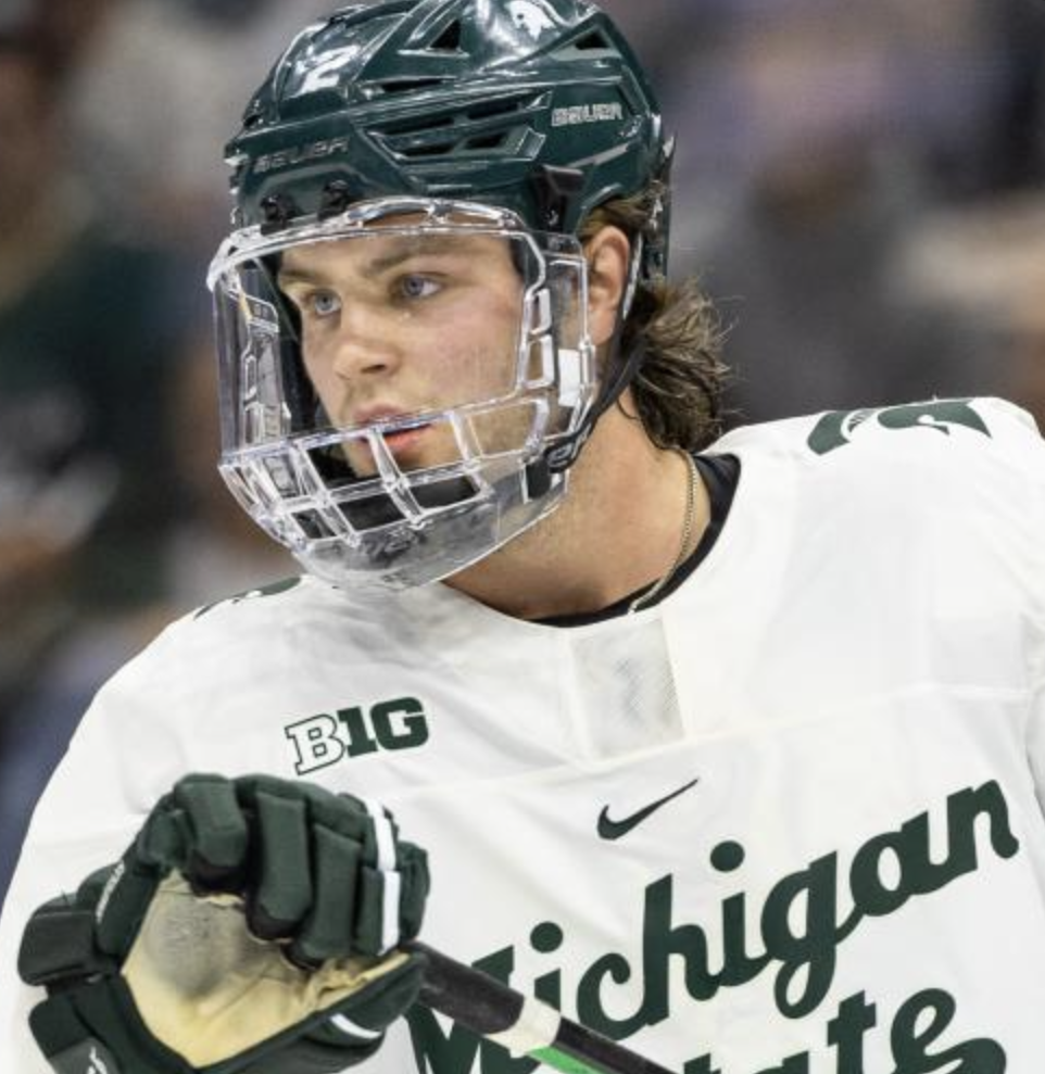 A male ice hockey player wearing a green helmet and white jersey with Michigan State University logo and Big Ten logo, holding a hockey stick.