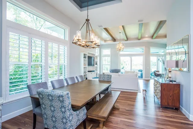 Open living and dining area with large windows, wooden dining table with chairs, a bench, white sofa, and modern lighting fixtures.