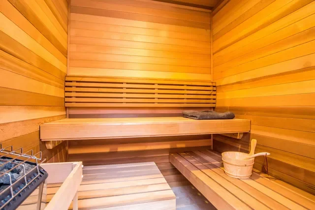 Interior of a traditional wooden sauna room with benches, a bucket, and a heater.
