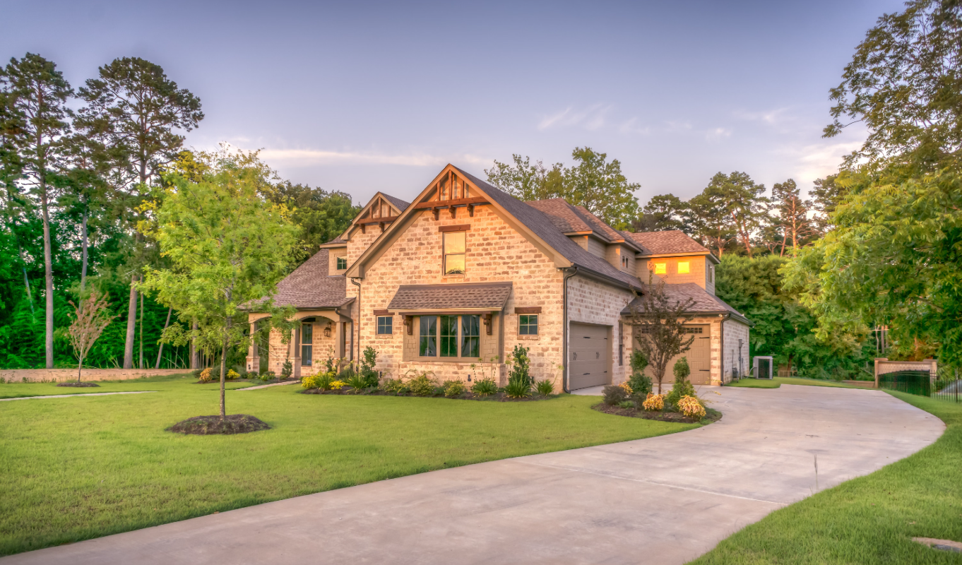 Large house with stone and wood exterior, surrounded by green lawn and trees, with a curved driveway.