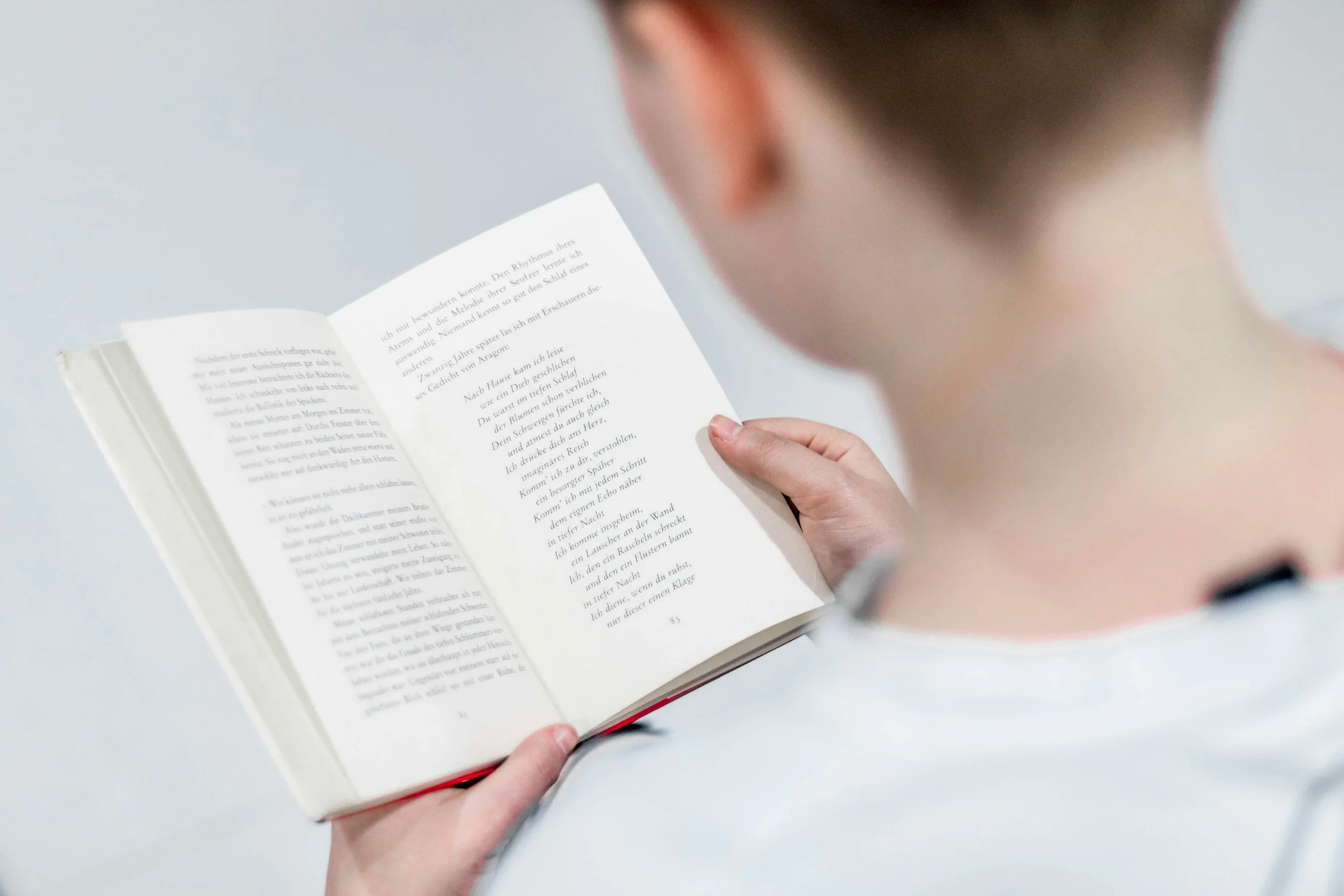 Person holding open book, close-up of hands, blurry person's head in foreground, white background.