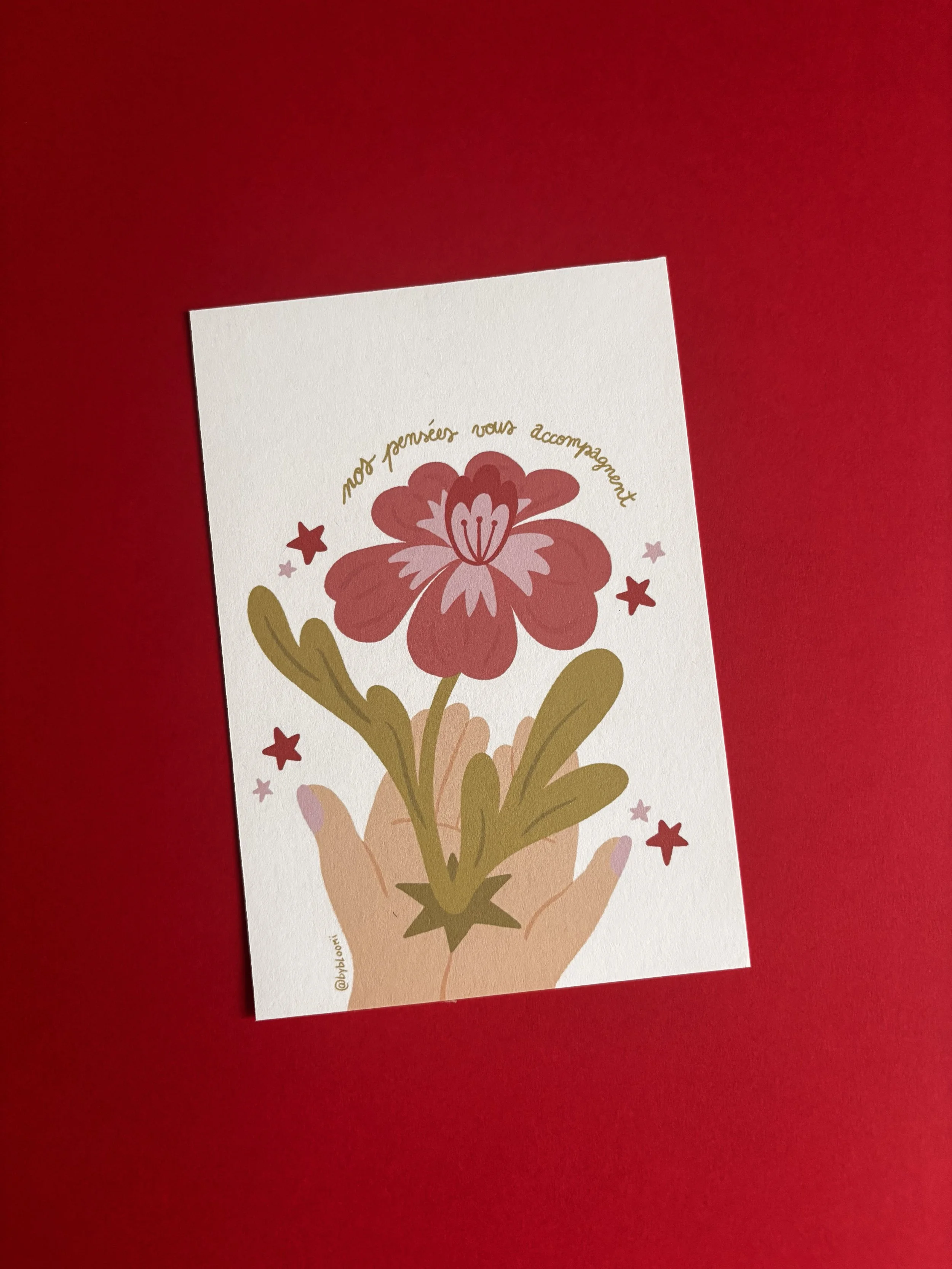 Carte de vœux avec une main tenant un bouquet de fleurs stylisées et le texte 'mes pensées vous accompagnent' en arc au-dessus du bouquet, sur fond blanc.