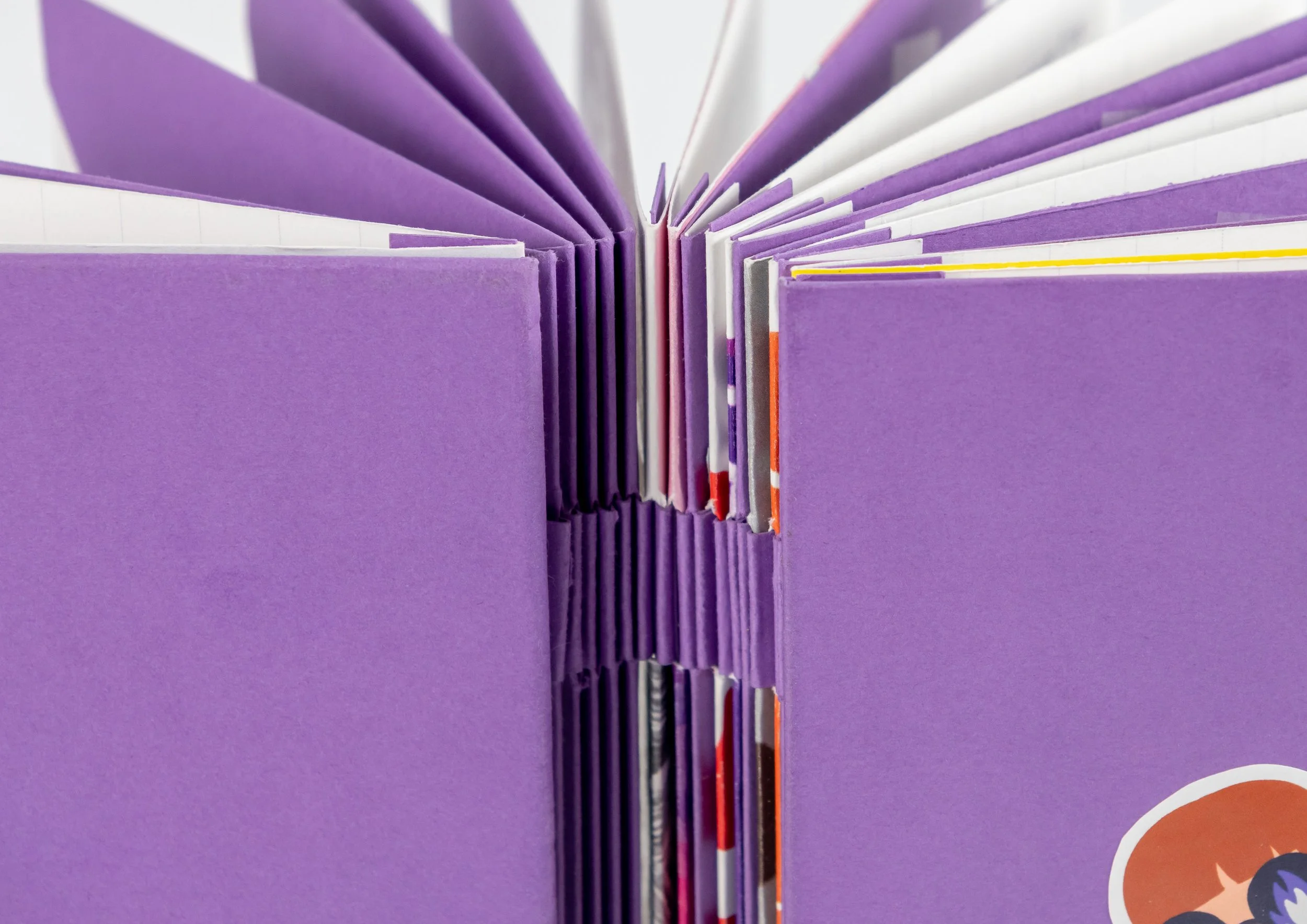 Livre ouvert avec des pages violettes, blanc, gris et colorées, avec une couverture violette, vu de devant.