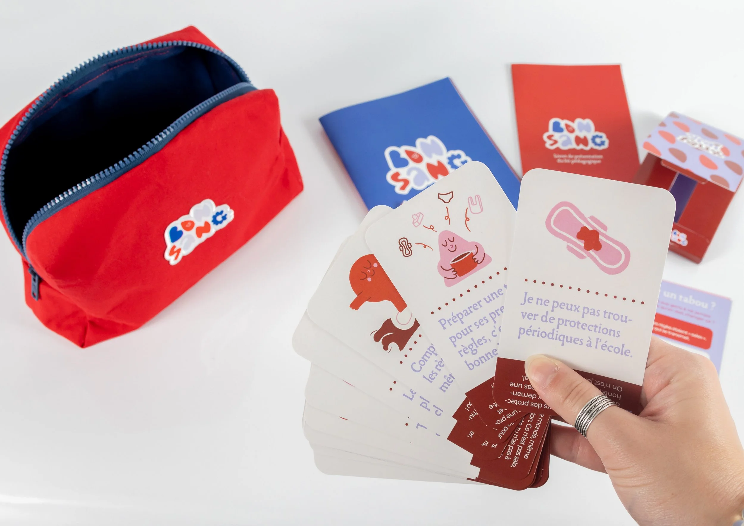 Jeune femme tenant des cartes avec des illustrations et du texte, à côté d'une petite sacoche rouge avec un logo coloré.