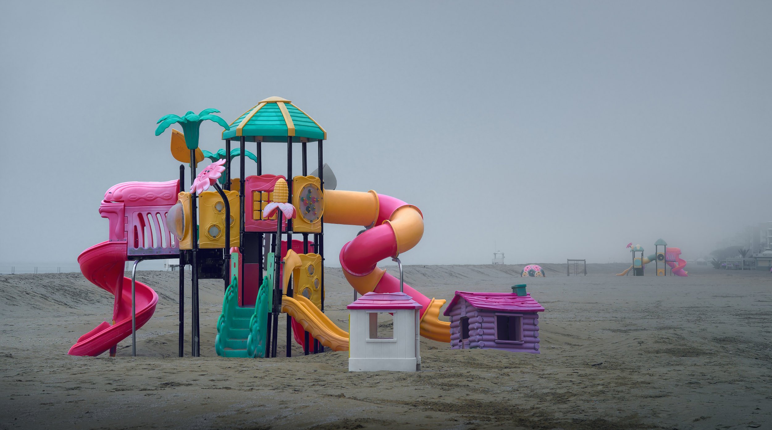Parco giochi colorato sulla spiaggia con nebbia e assenza di persone.