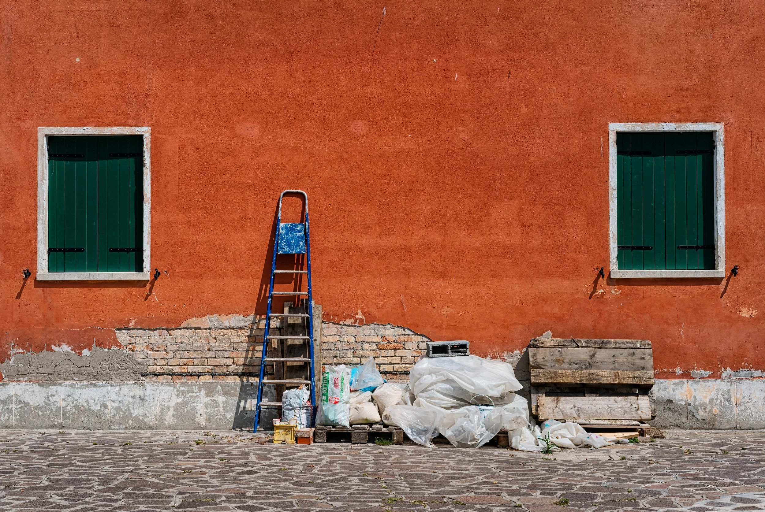 An orange wall in Burano, marked by contrasting architectural details and strong sunlight.