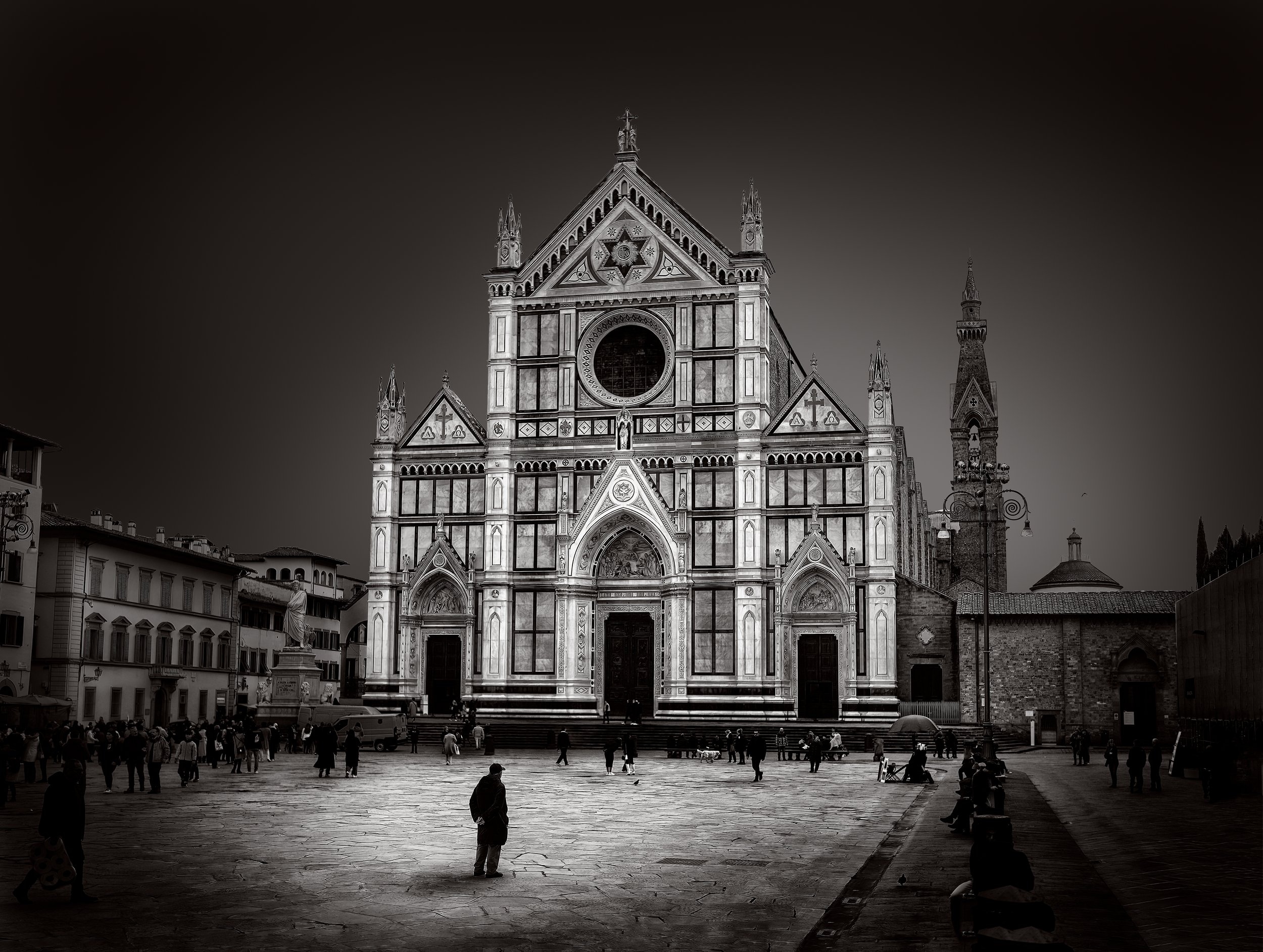 La chiesa di Santa Maria del Fiore con la facciata in marmo bianco, rosa e verde e il campanile accanto, situata in una piazza affollata con persone e alcune statue.