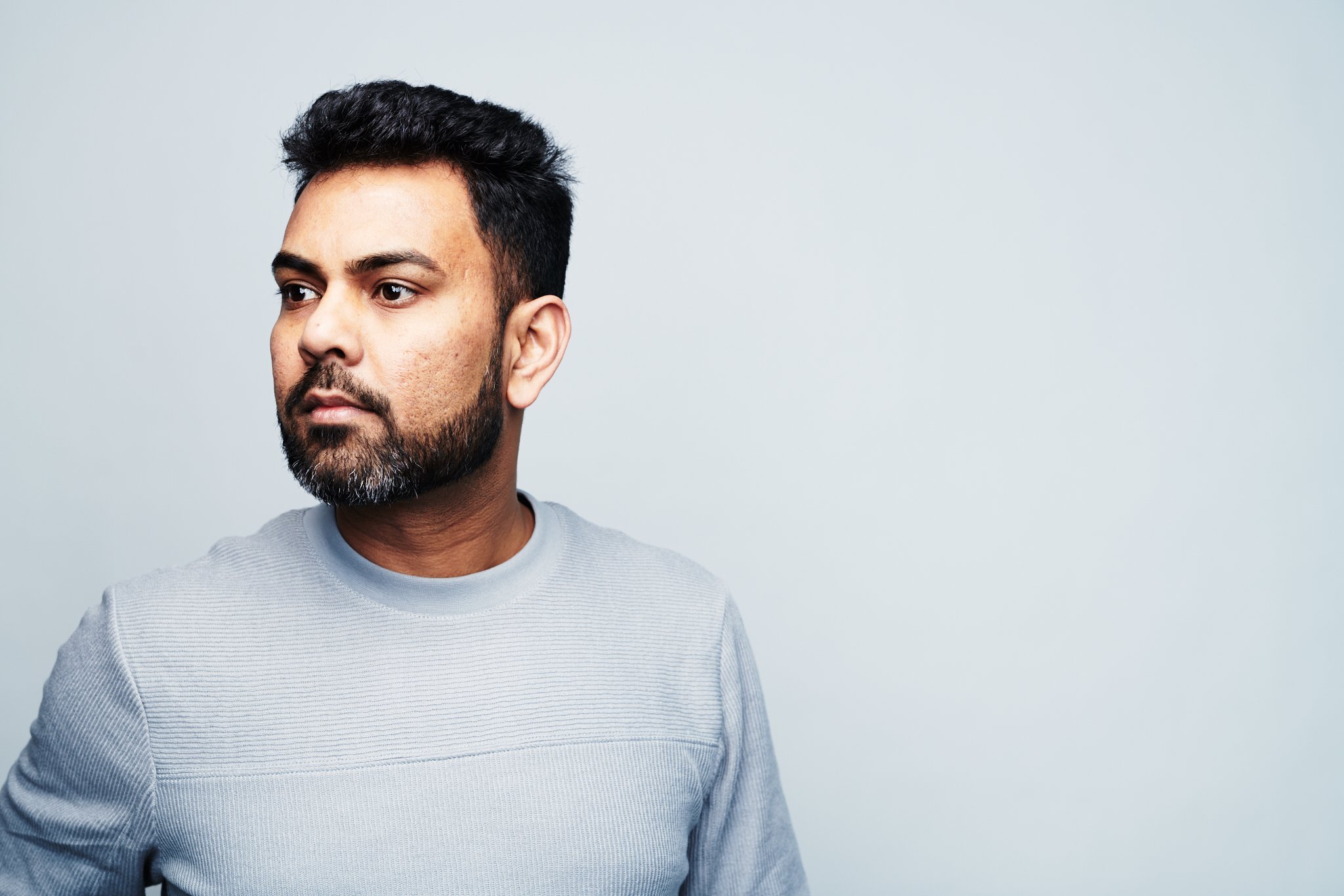 Praveen Sake wearing a light gray long sleeve shirt, looking to the side against a plain light background.