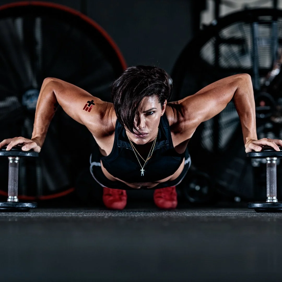 Female athlete in gym doing push-ups on weighted bars.