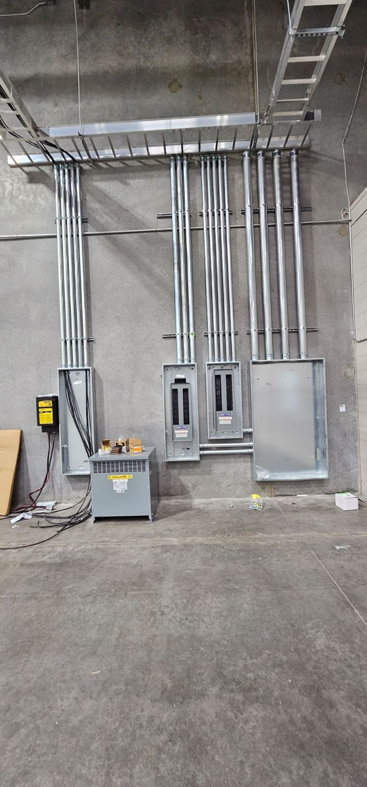 Electrical wiring and panels installed on a concrete wall, with metal conduit pipes leading to electrical boxes.