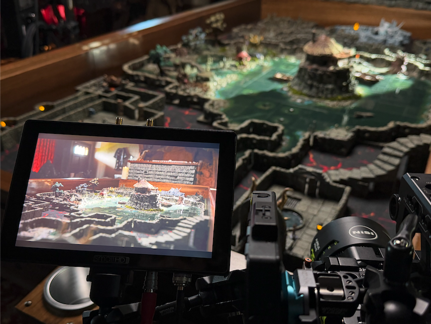 A detailed miniature model of a landscape with water, structures, and pathways showcased under a camera viewfinder.