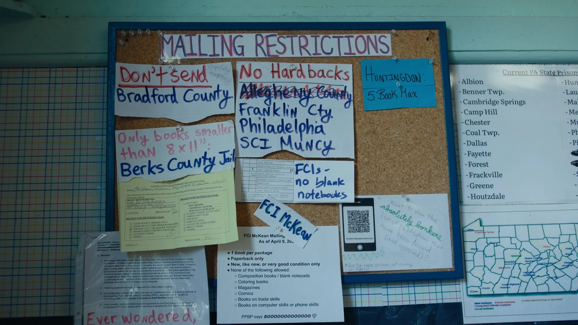 Bulletin board with mailing restrictions notices and various papers, including Xeroxed lists, handwritten notes, and a QR code, in a community center or office.