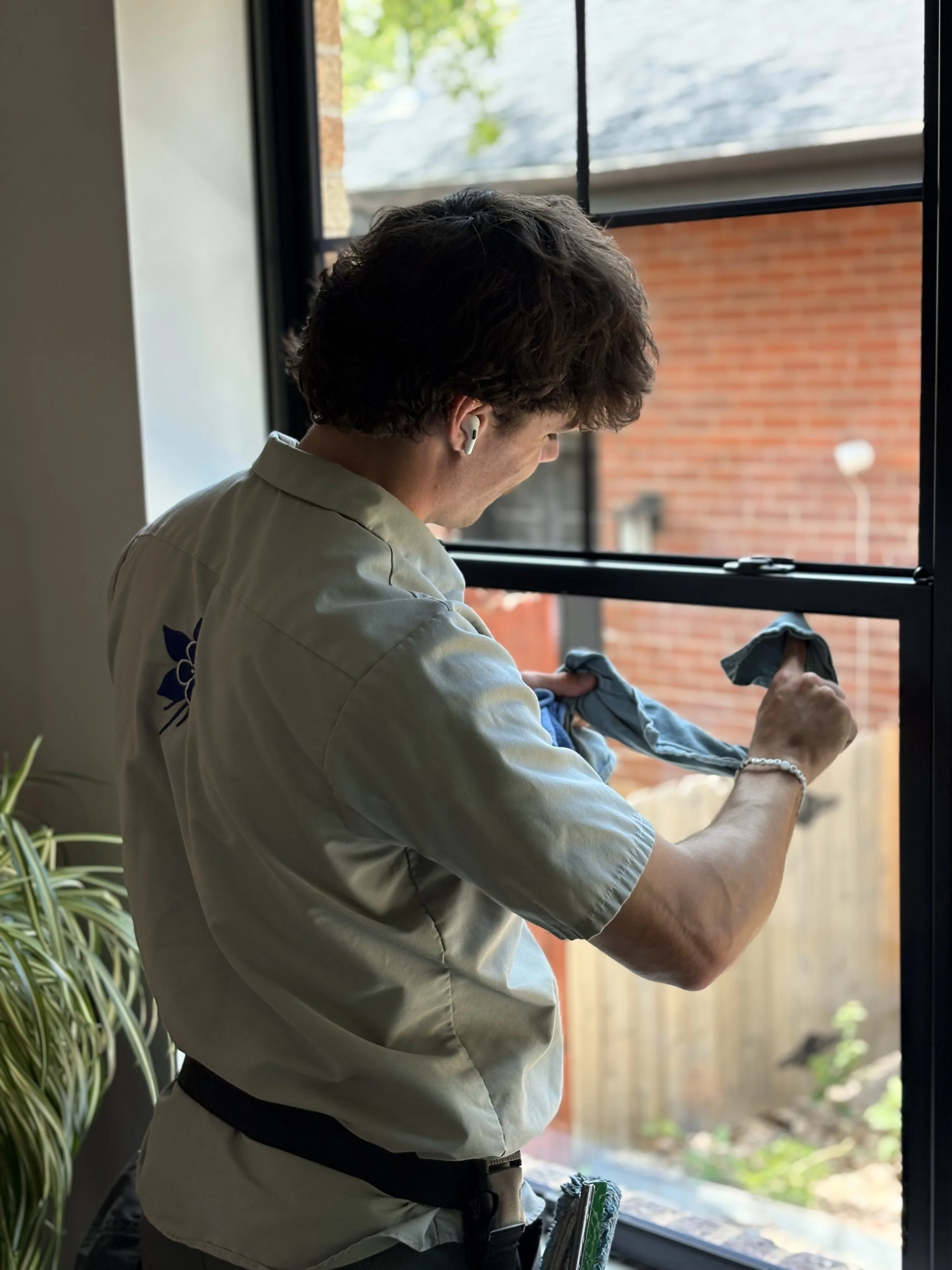 A technician wearing a company Columbine Window Cleaning shirt, detailing a window.