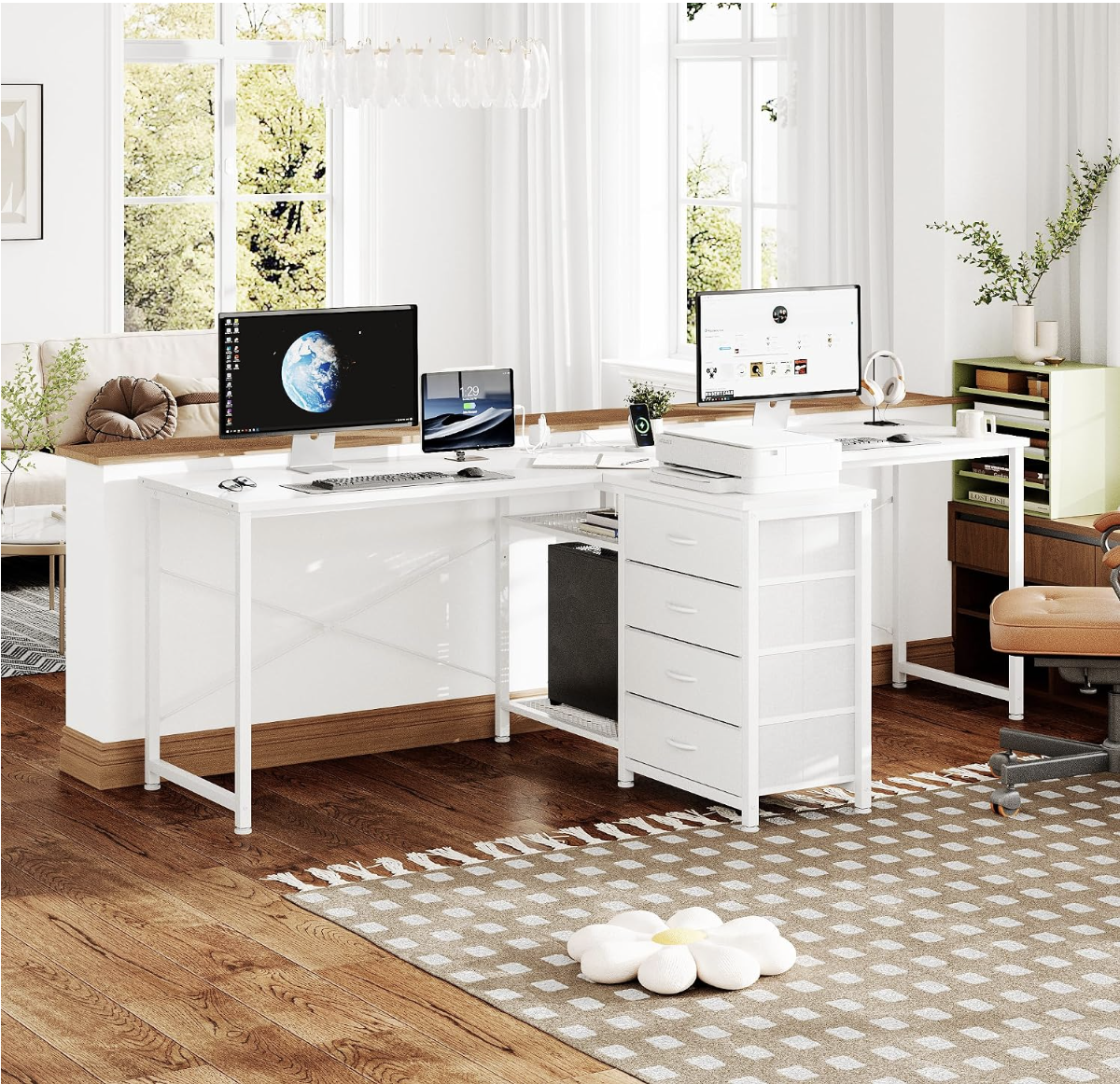 Bright home office with two computer monitors on a white desk, an ergonomic chair, and natural light from large windows with white curtains, decorated with indoor plants and a patterned rug.