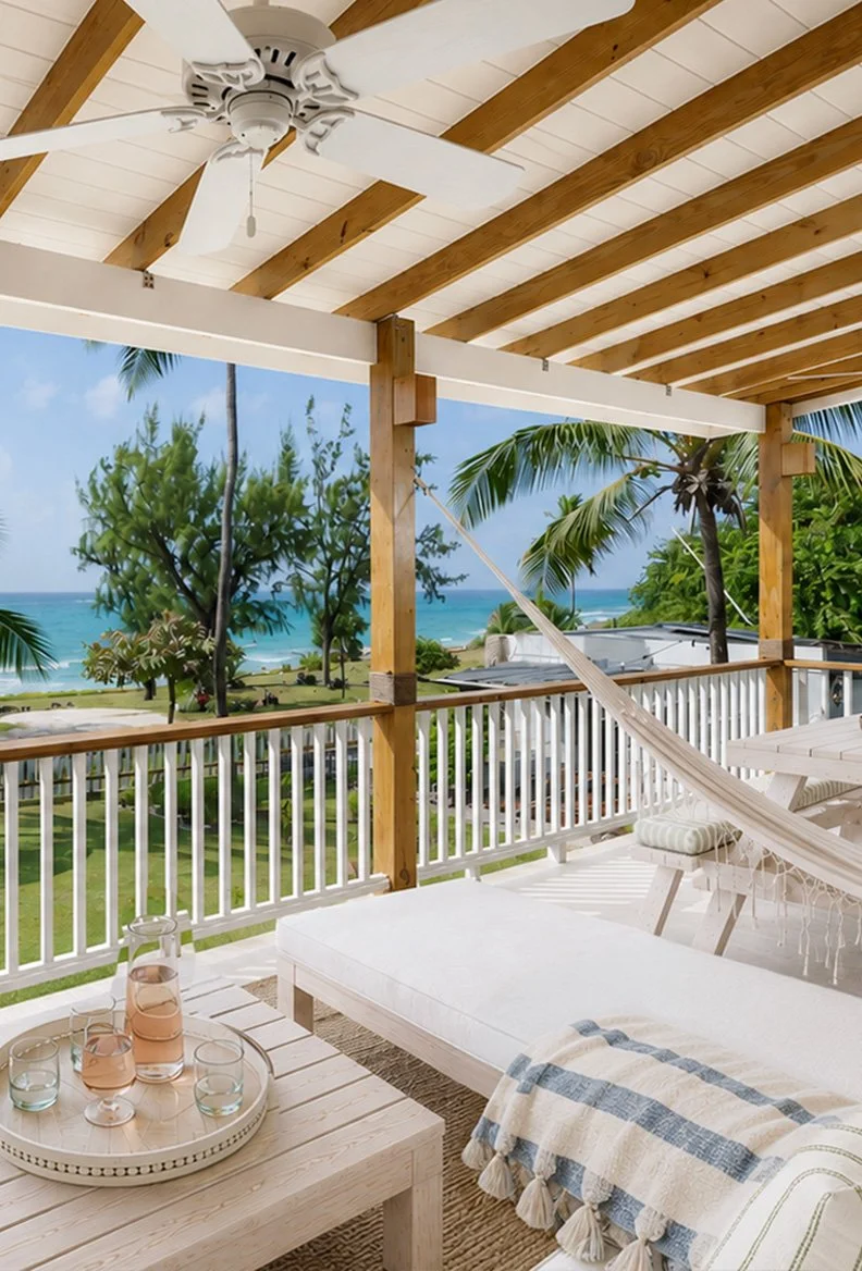 Beachside porch with white wooden furniture, a hammock, and lush tropical trees and palm trees overlooking the ocean.
