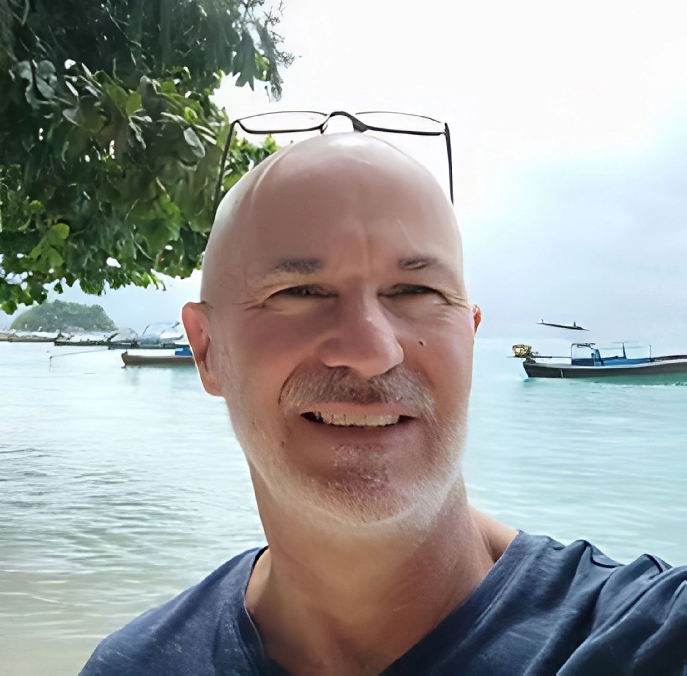 Martin Knights wears a blue shirt and stands in front of the ocean