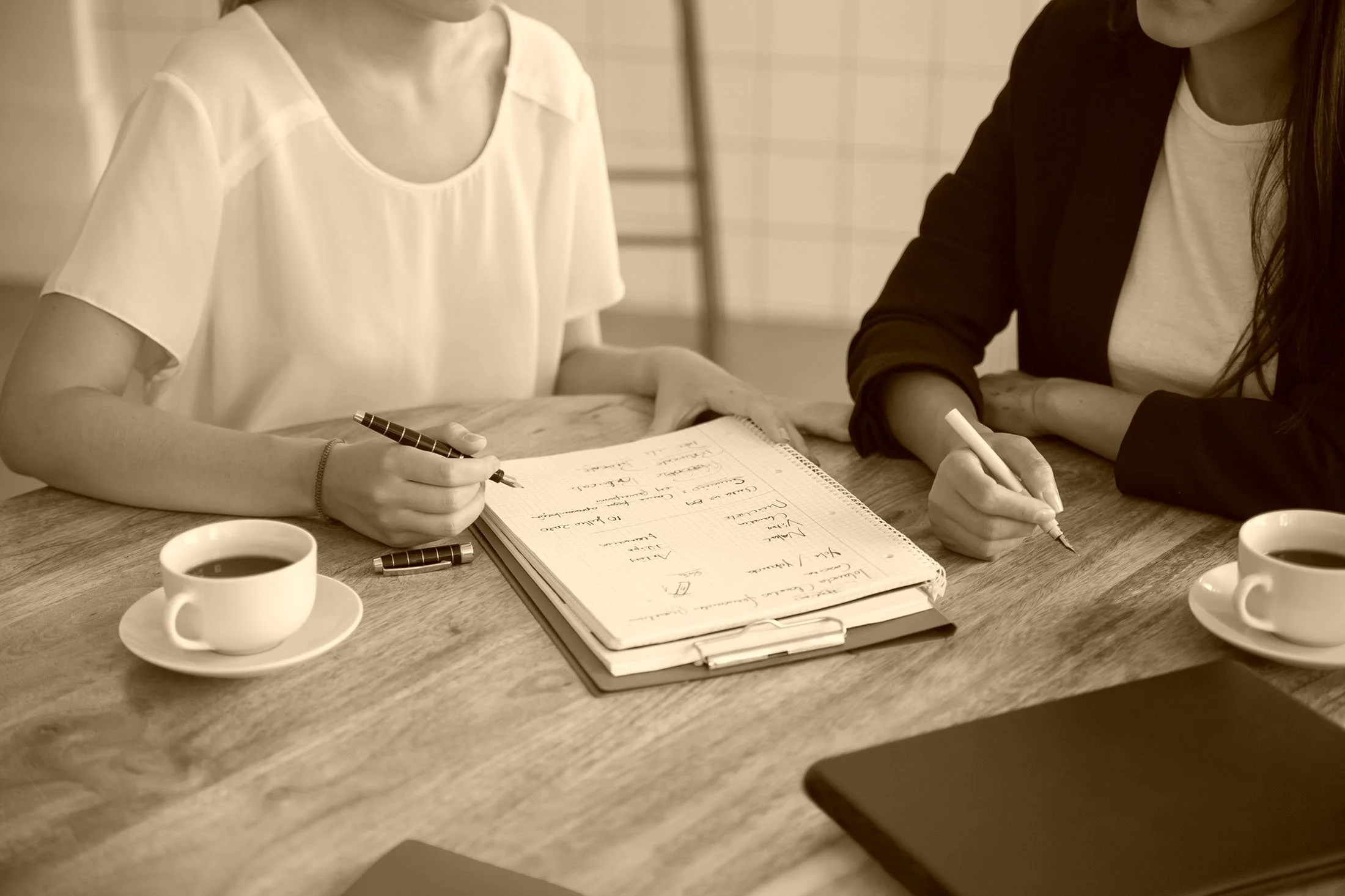 Women brainstorm with a notebook and coffee