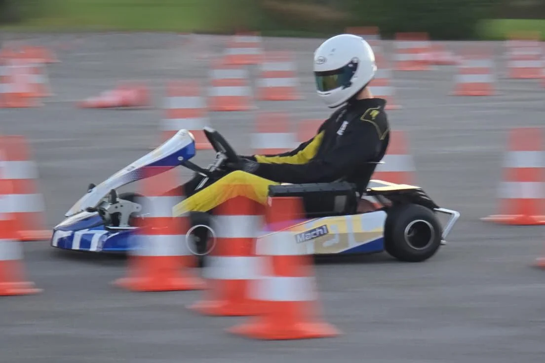 Mann fährt mit einem Go-Kart durch eine Slalom-Strecke mit orangefarbenen Verkehrshelmen.