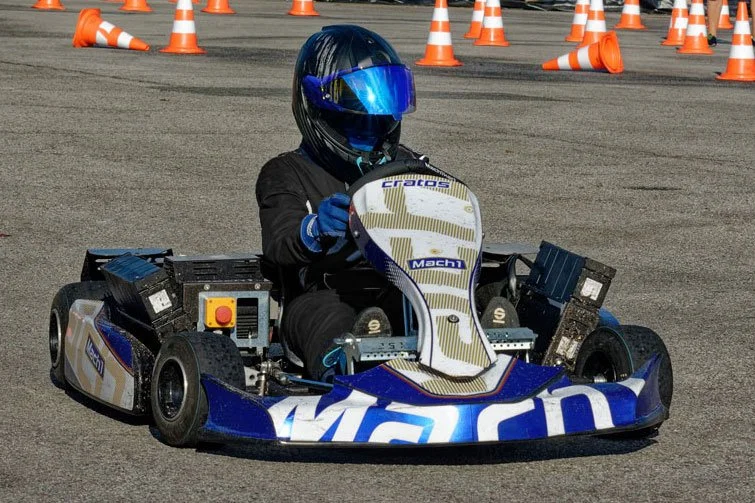 Eine Person fährt in einem Go-Kart auf einer Strecke mit orangenen Verkehrsampeln und Verkehrshütchen.