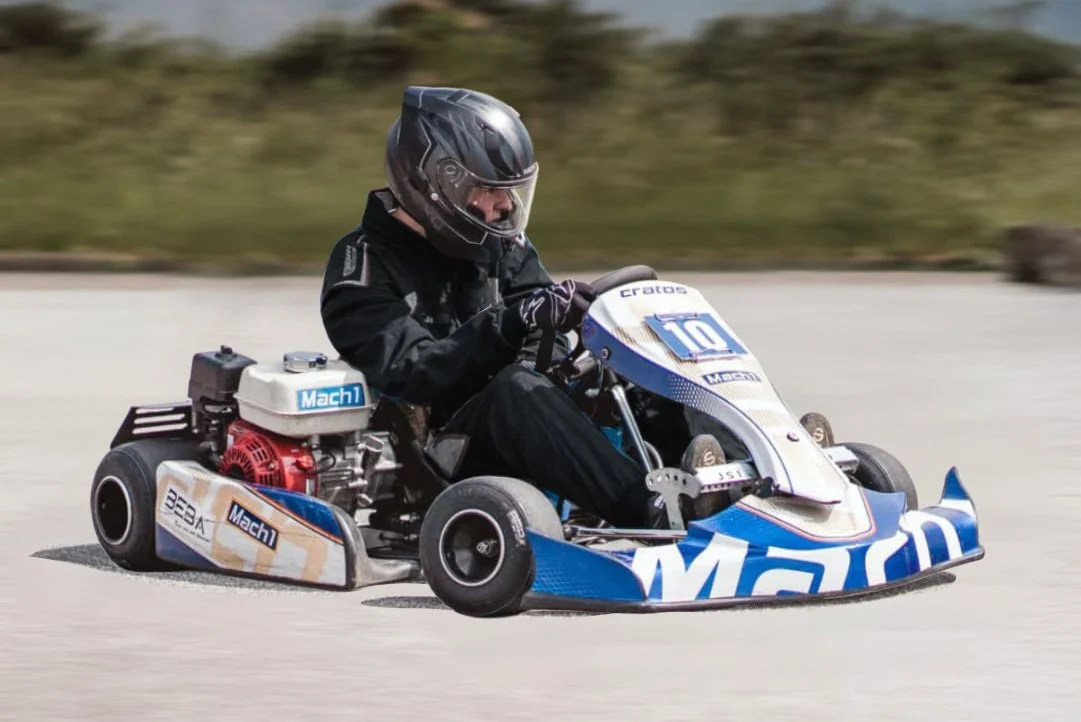 Ein Mensch fährt in einem go-kart auf einer Strecke, trägt einen Helm und schwarze Kleidung.