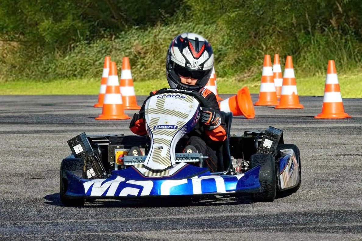 Ein Junge fährt auf einem Go-Kart auf einer Rennstrecke, umgeben von orangefarbenen Verkehrszeichen.