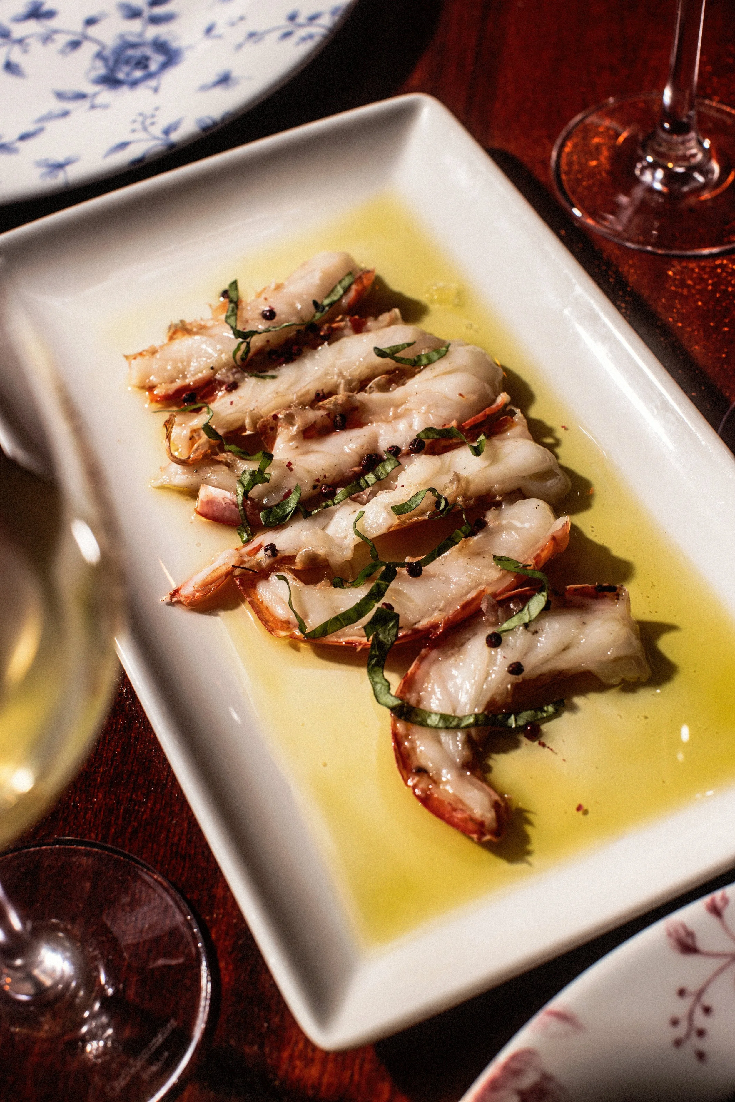 Shrimps garnished with herbs, served on a white rectangular plate, with a glass of red wine nearby.