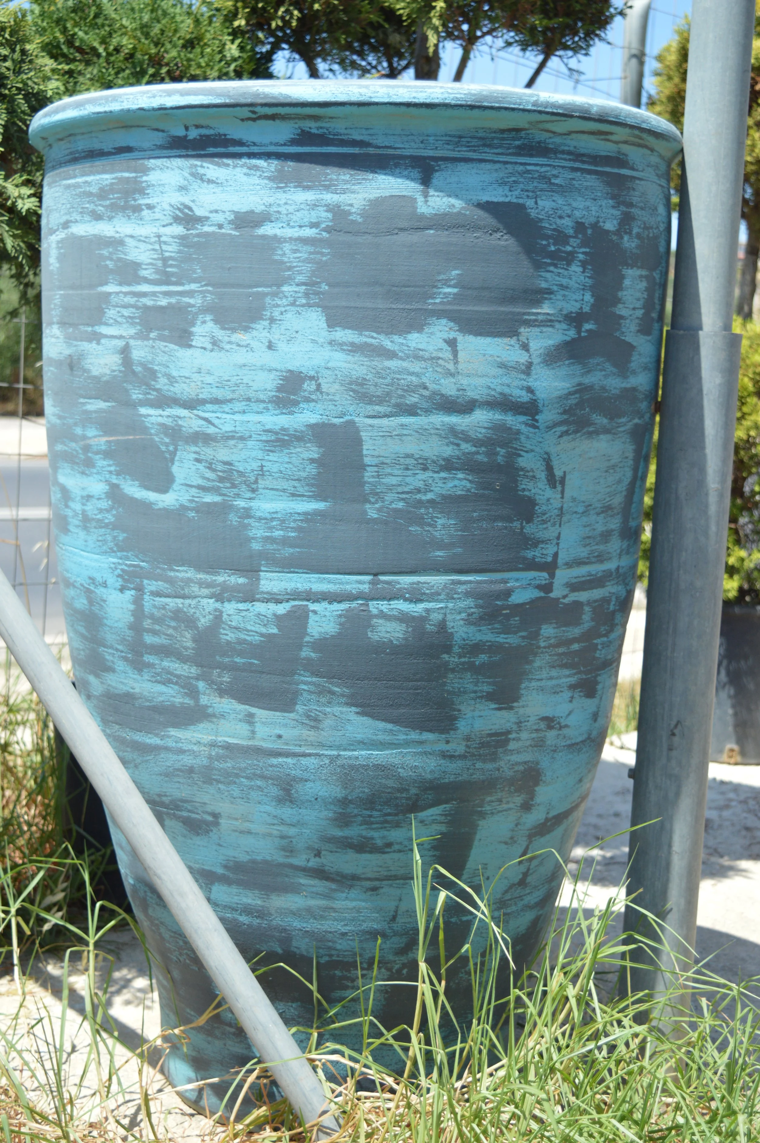 Large blue weathered outdoor planter with a distressed paint finish, surrounded by grass and located near a metal pole and fence.