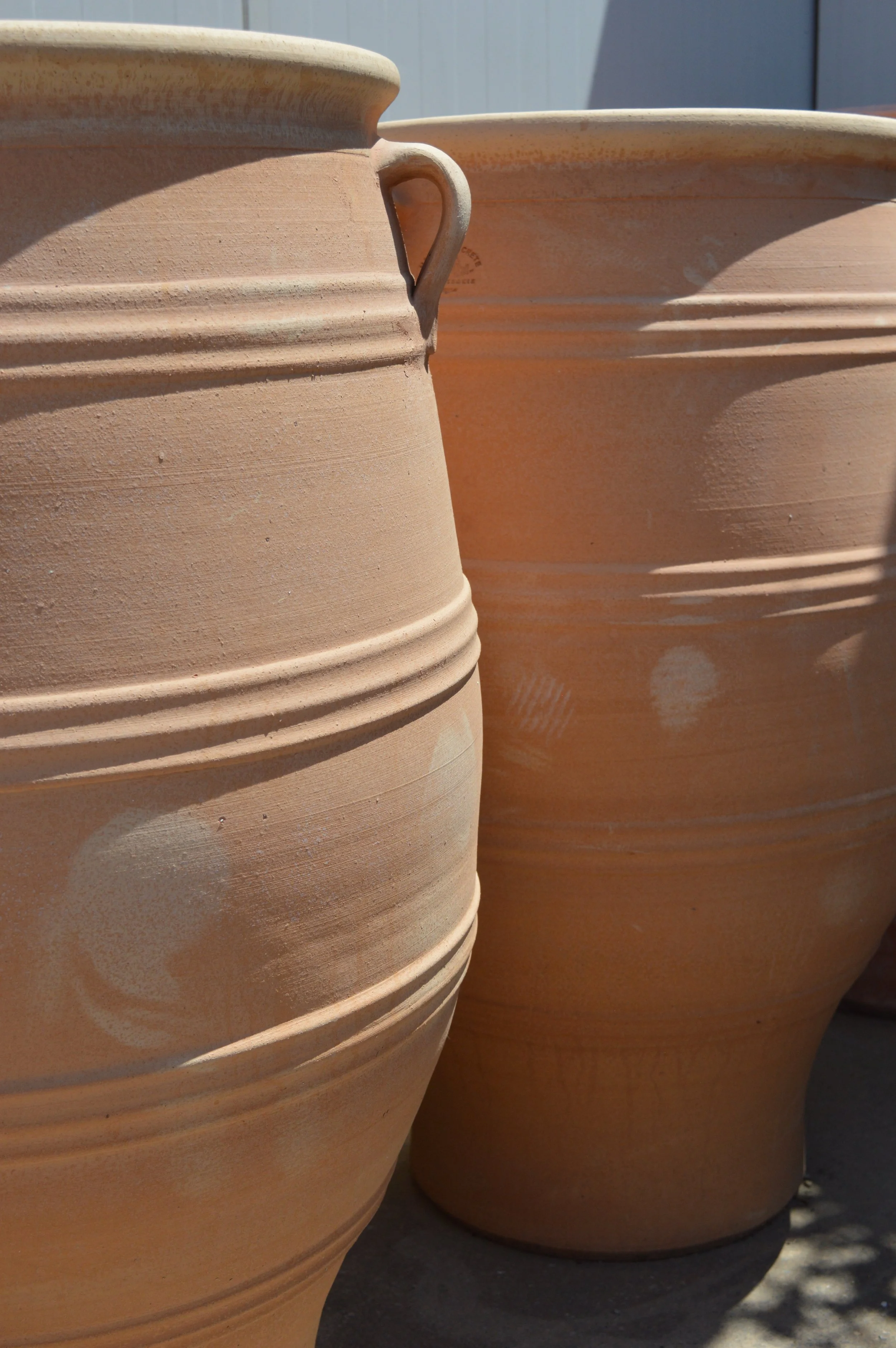 Close-up of large terracotta plant pots with ridges, outdoors, with a blue fence in background.