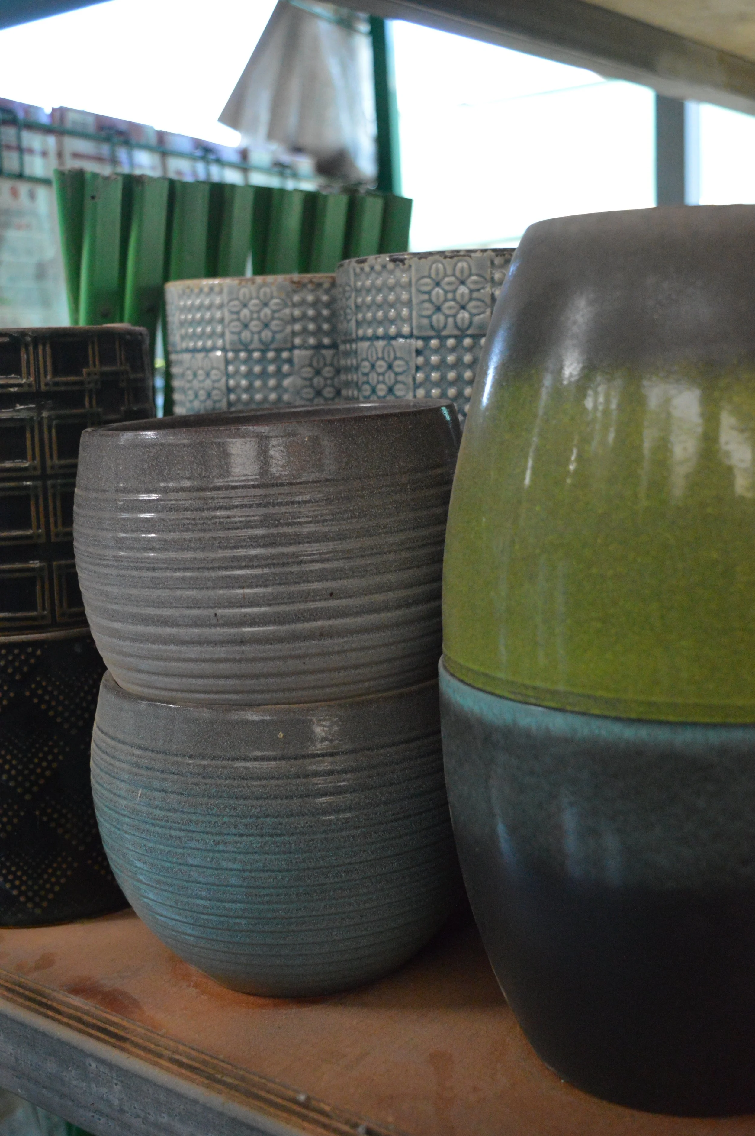 Close-up of various ceramic pots and bowls in different colors and textures, stacked on a wooden surface.