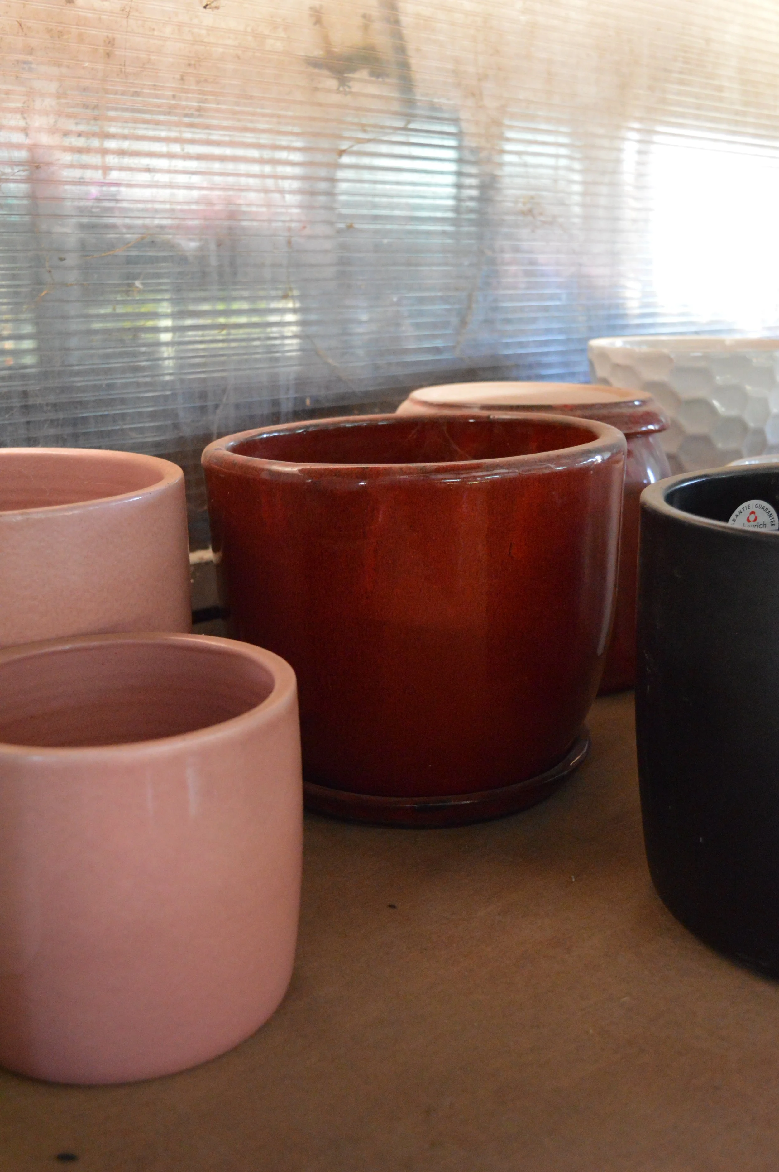 Several ceramic pots of different colors and sizes on a shelf with a reflective surface behind them.