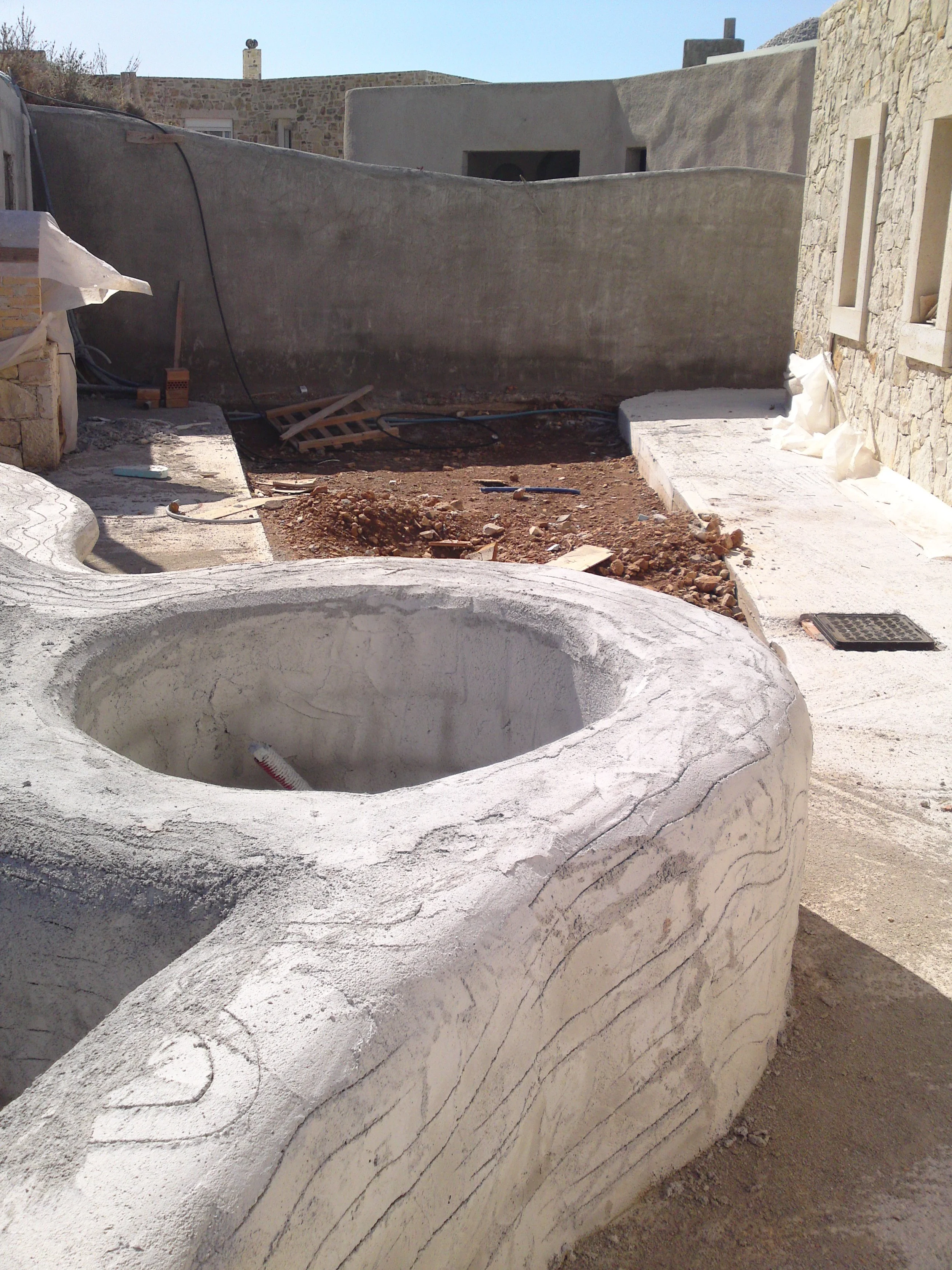A construction site with a white concrete bathtub in the foreground and a stone and concrete building in the background.