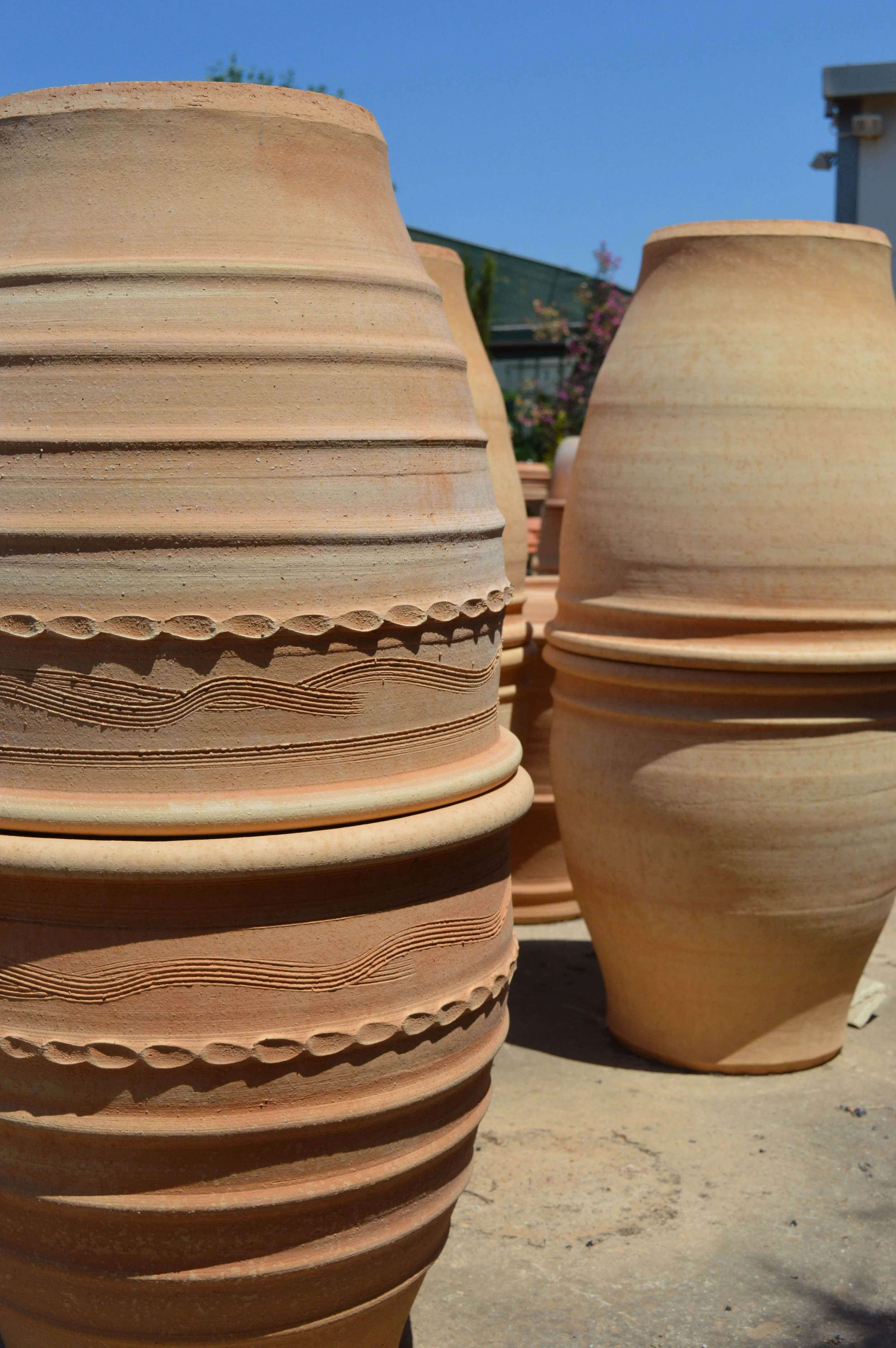Large terracotta flower pots with decorative patterns stacked outdoors under a clear blue sky.