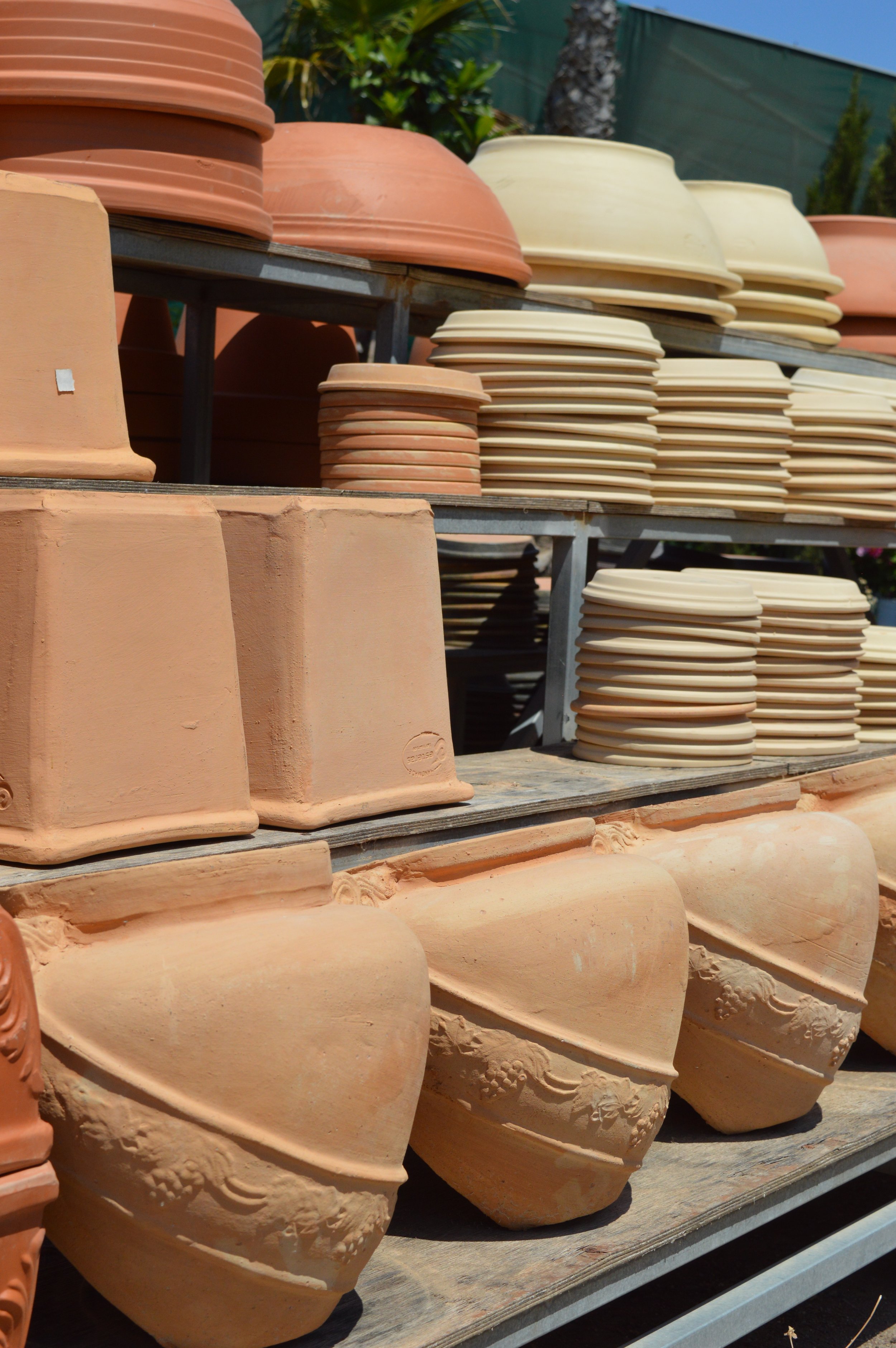 Clay pots and planters in various sizes and shapes on display outdoors, with some stacked and others arranged on shelves.