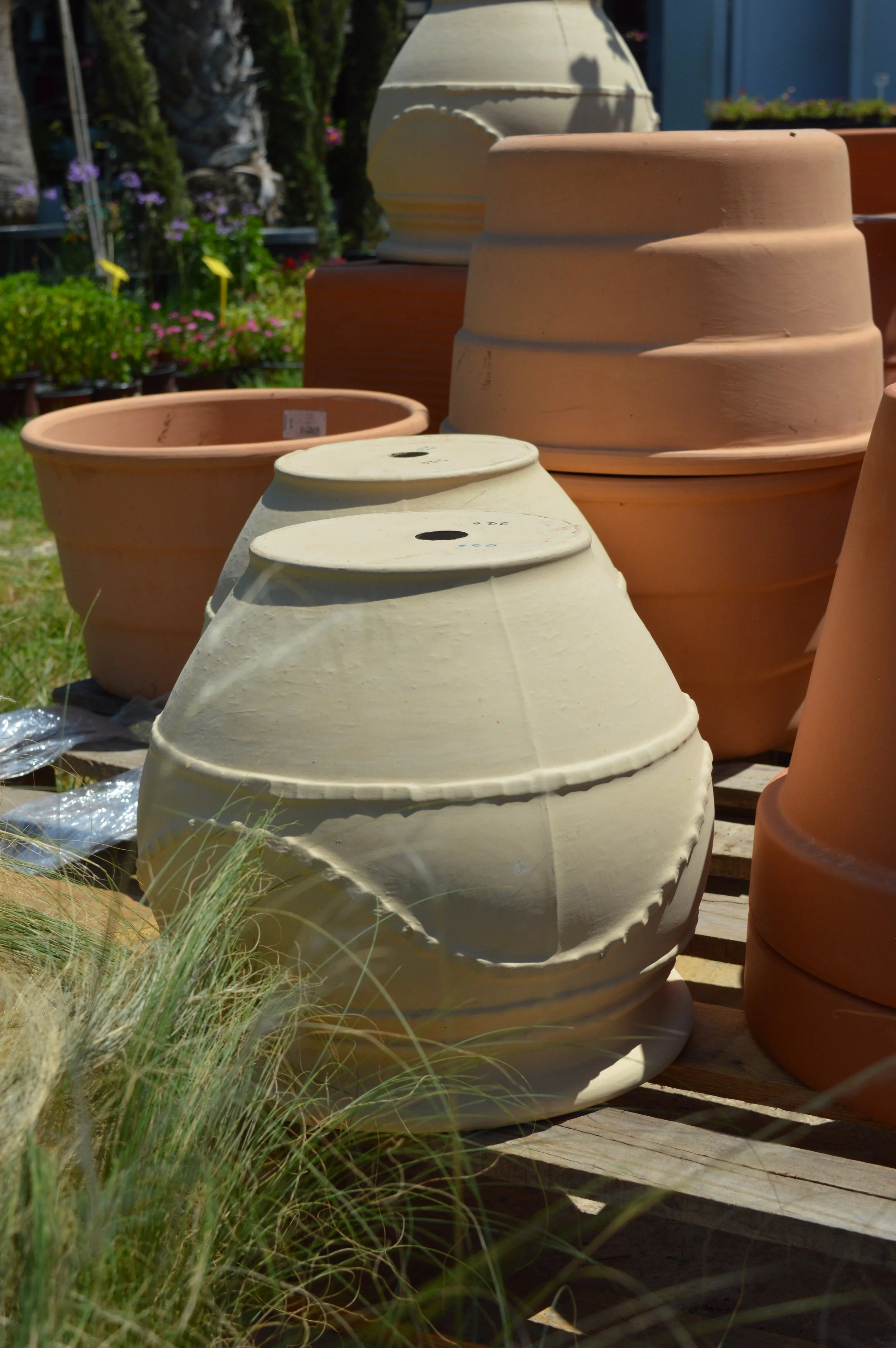 Various empty flower pots of different sizes and colors, placed outdoors on a wooden surface, with some plants and greenery in the background.
