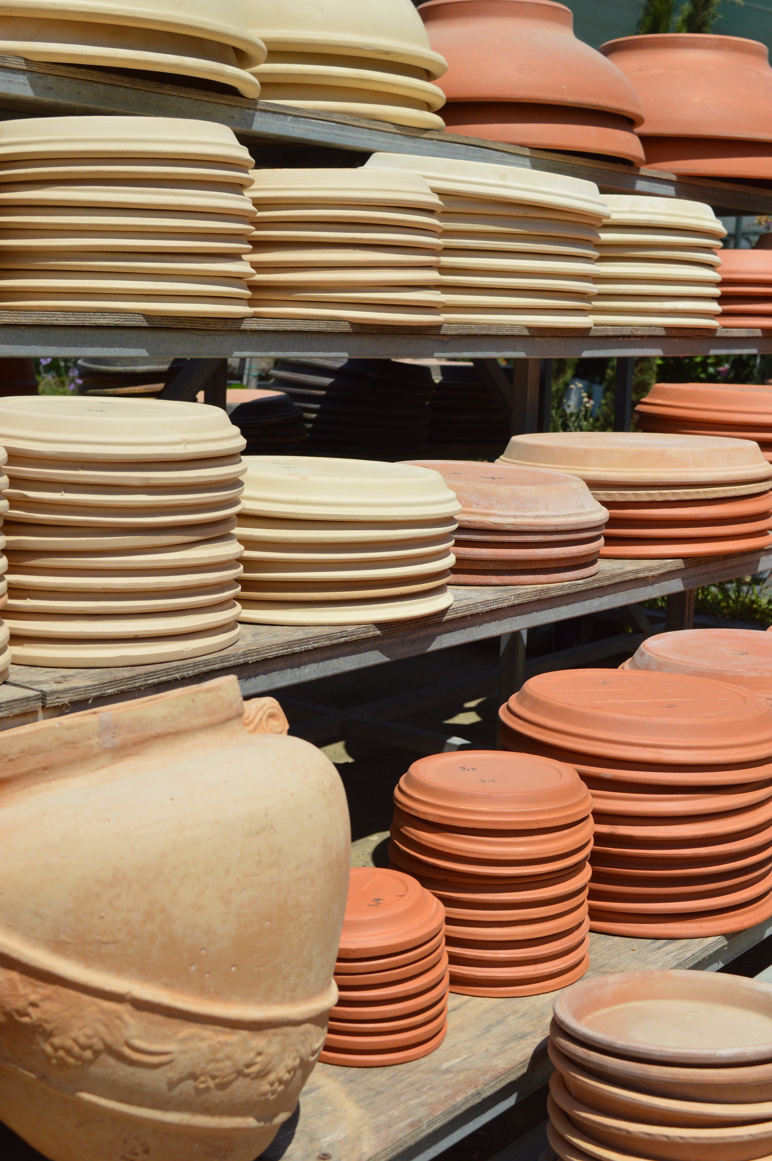 Stacks of unglazed pottery and clay pots on outdoor shelves.