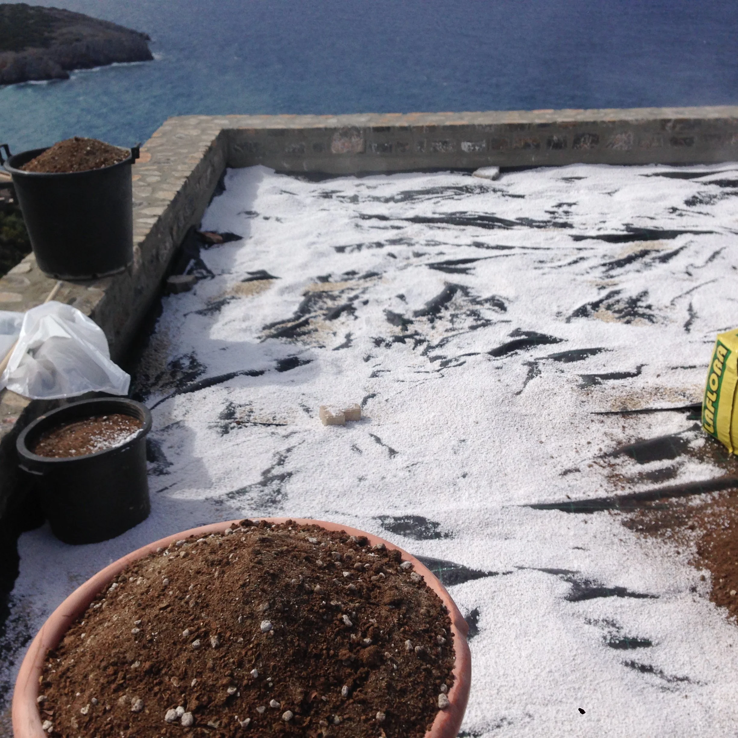Close-up of a terracotta pot filled with soil, placed outdoors on a snowy surface with other gardening supplies nearby.