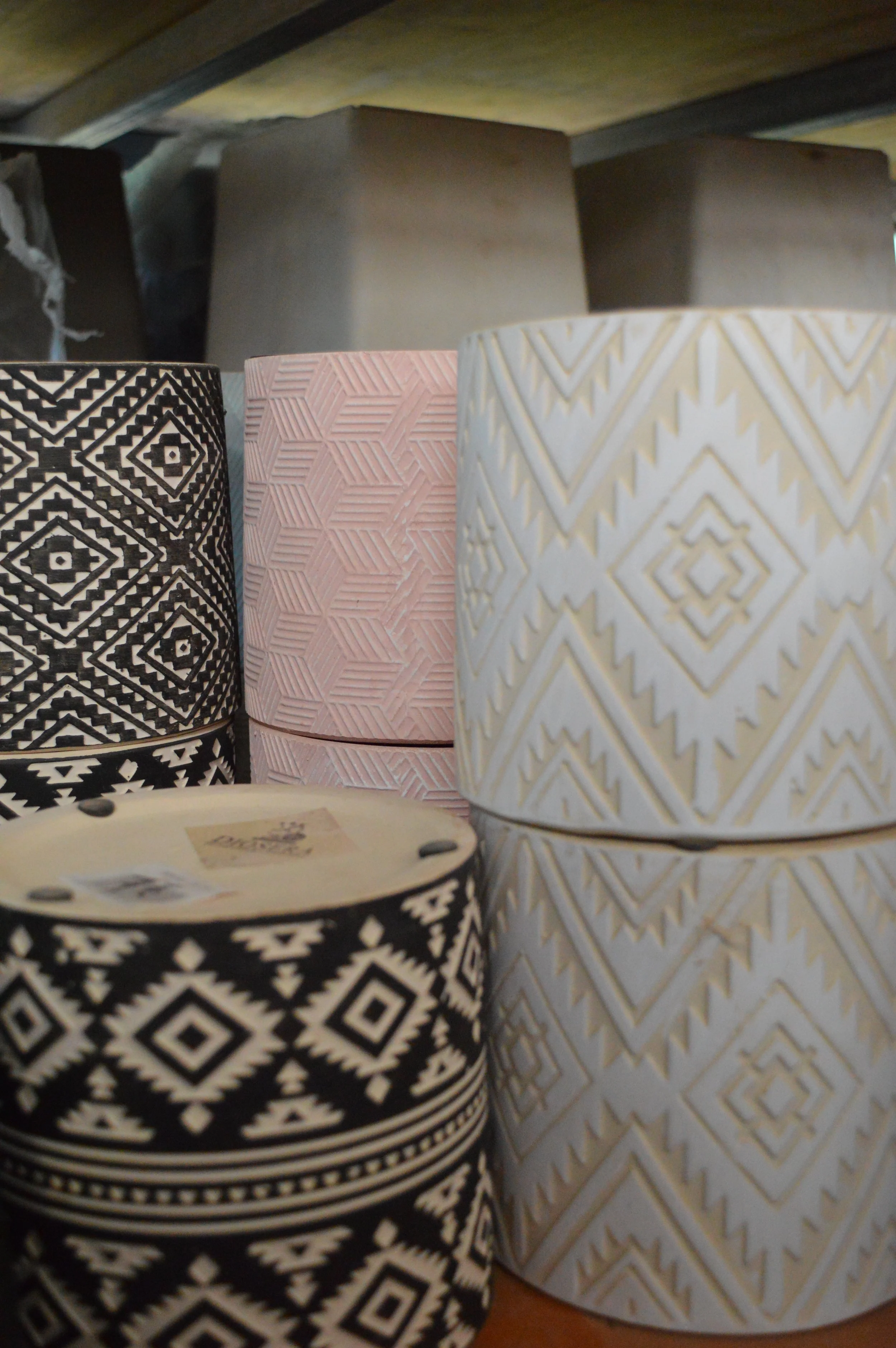 Stacked patterned cylindrical containers in black, pink, and white with geometric designs on a shelf.