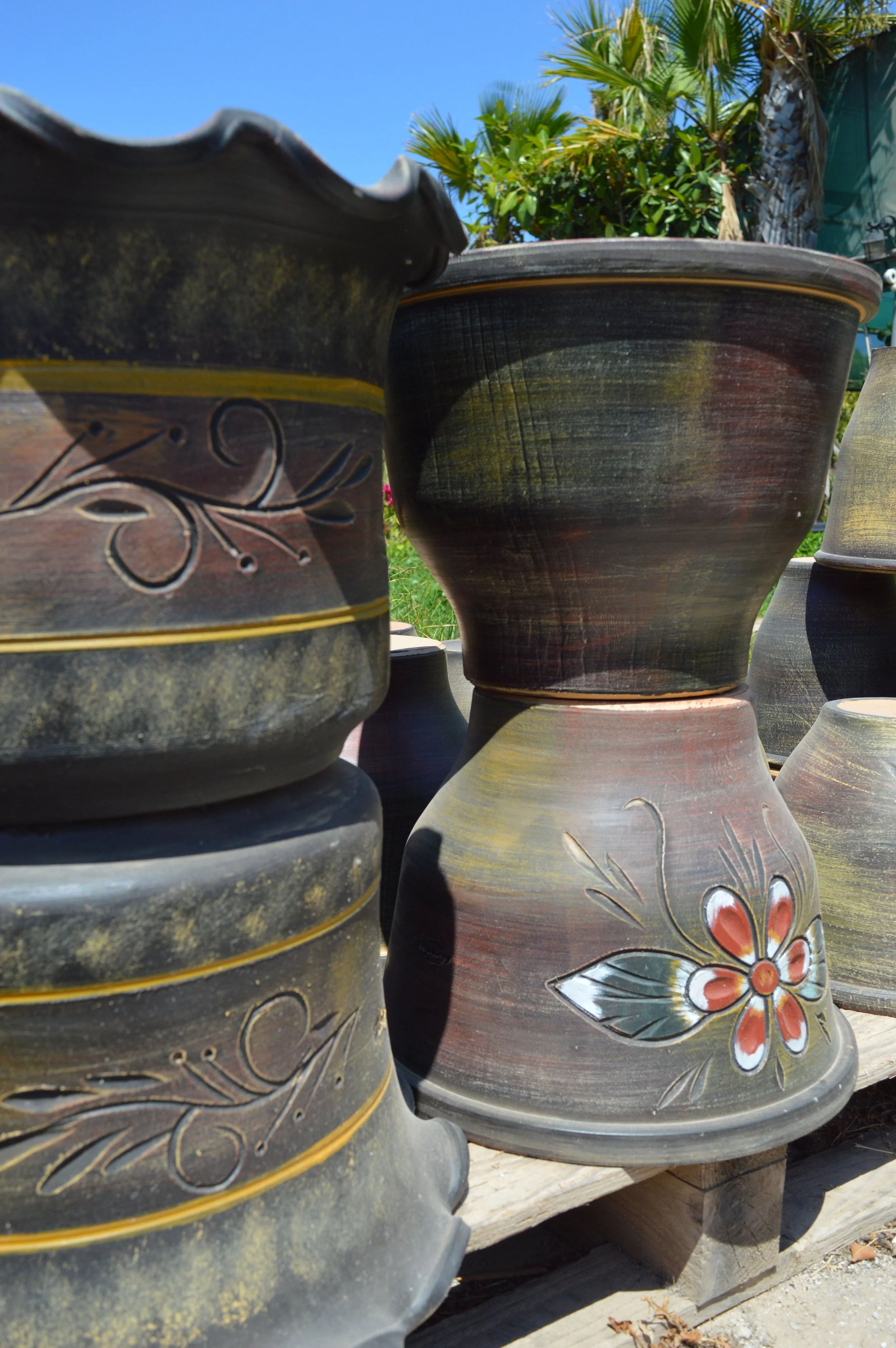 Close-up of colorful ceramic planters with floral and butterfly designs, outdoors with bright blue sky and palm trees in background.