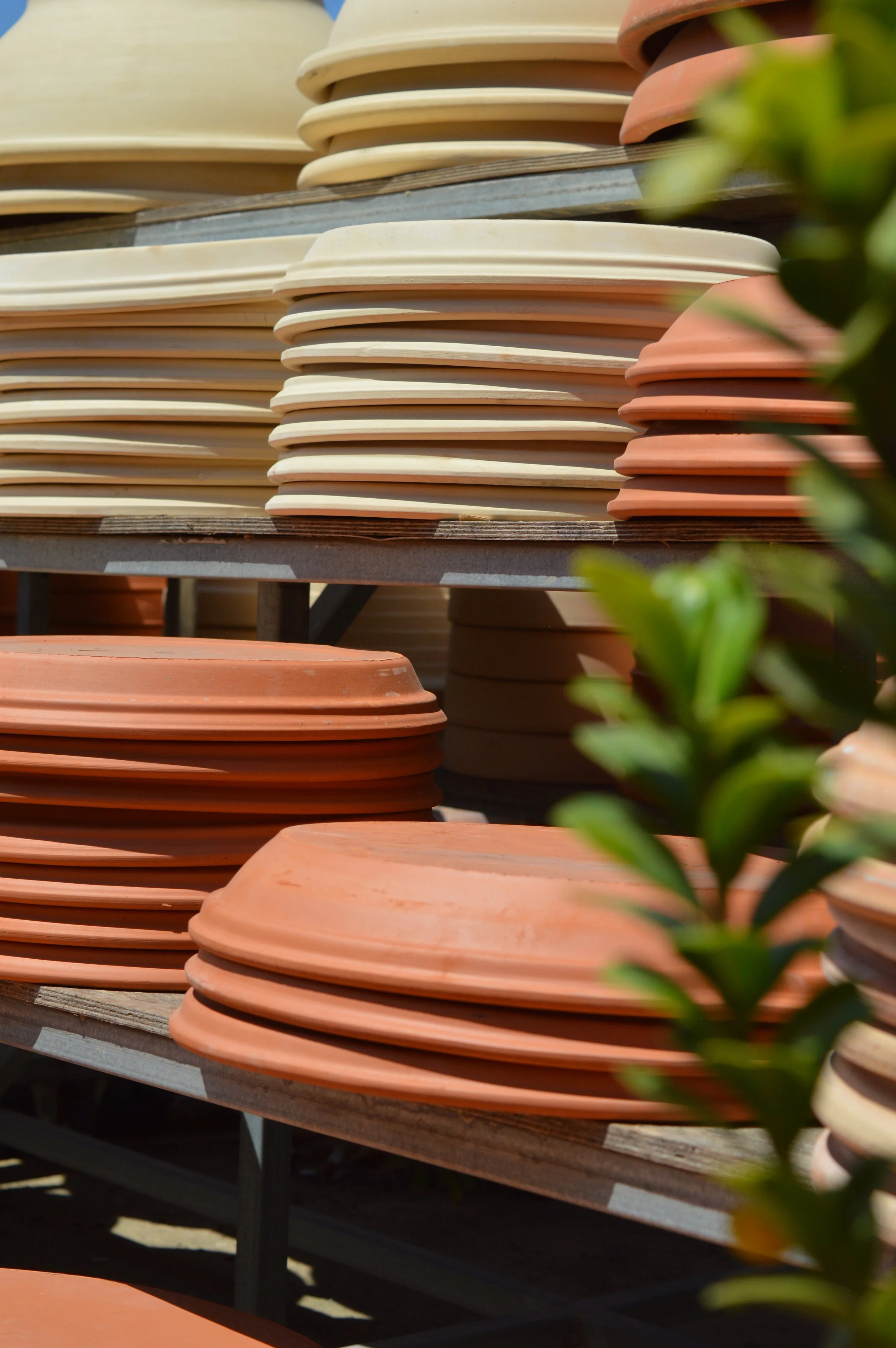 Stacked terracotta and cream-colored clay flower pots on shelves with blurred greenery in the foreground.